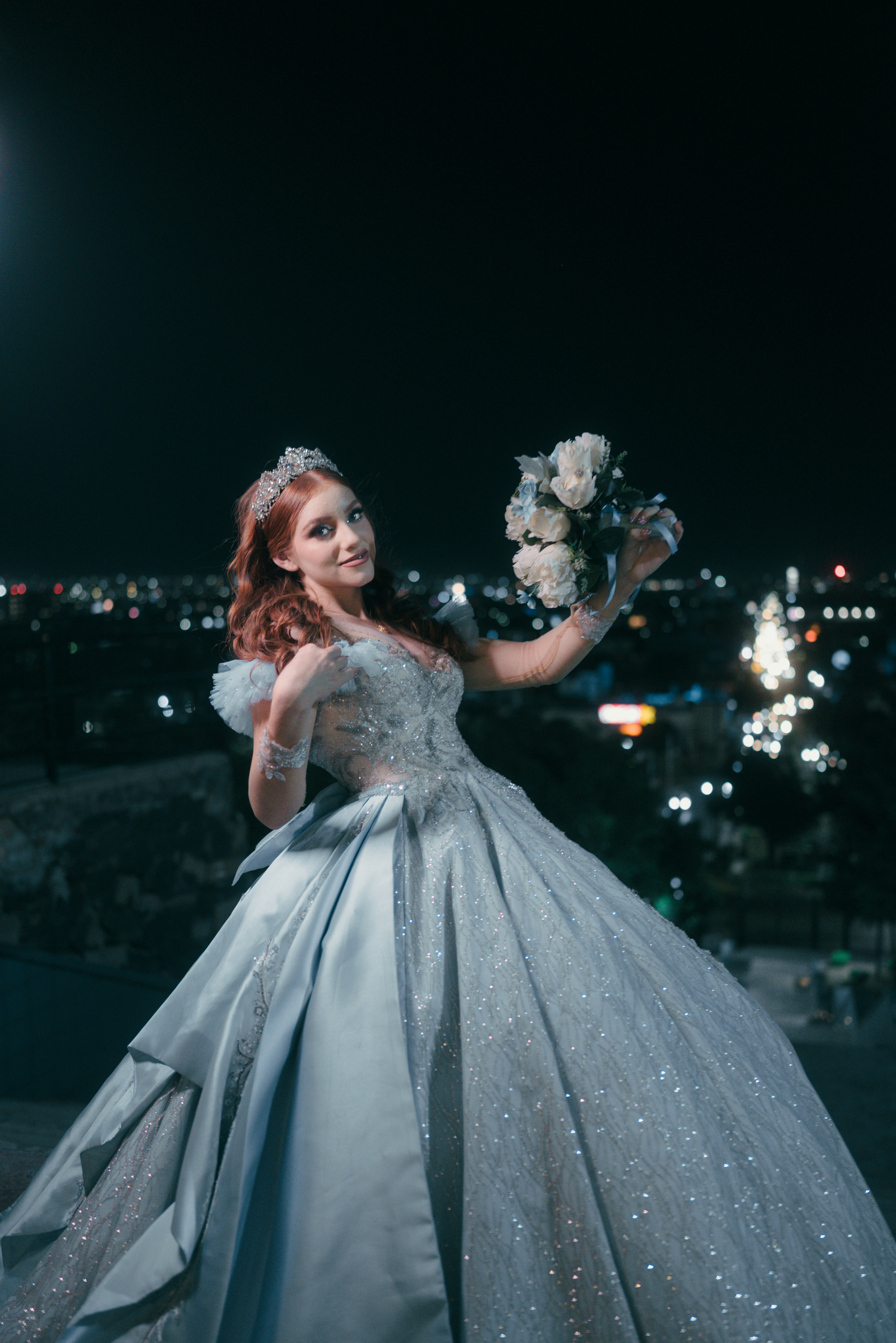 Young woman in a ballgown holding a bouquet at night.