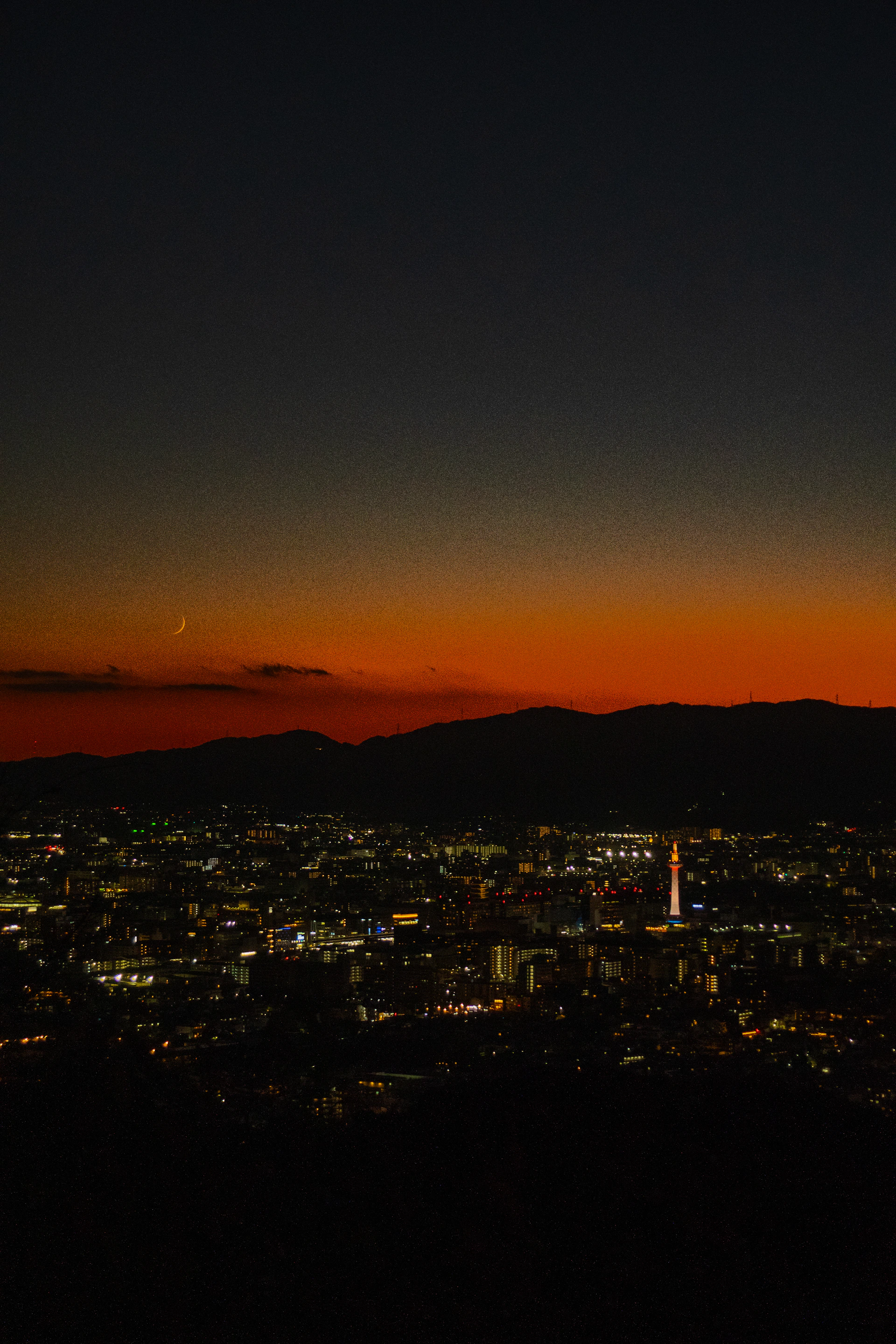 City lights glow under a twilight sky with crescent moon.