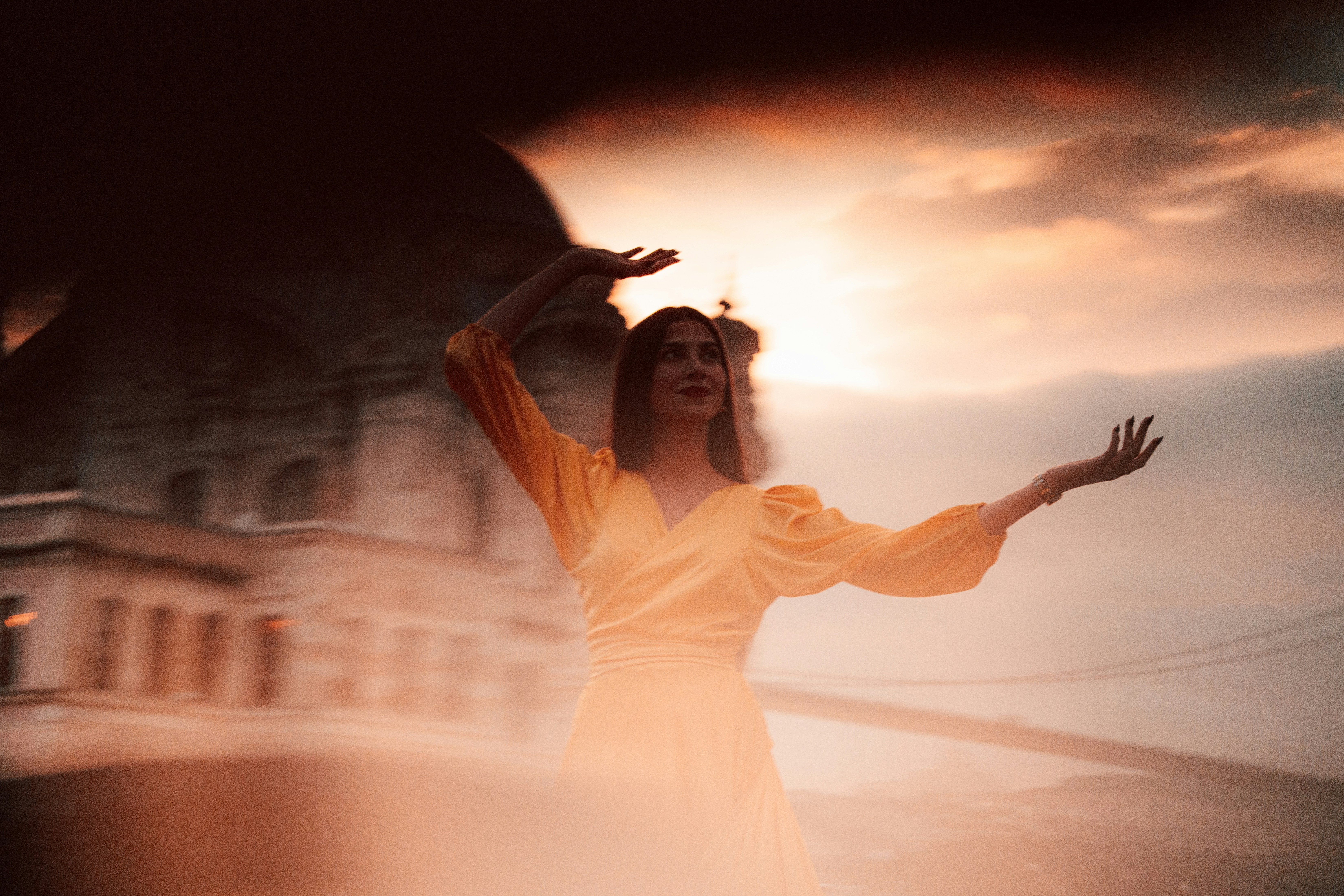 Woman in yellow dress with arms outstretched at sunset.