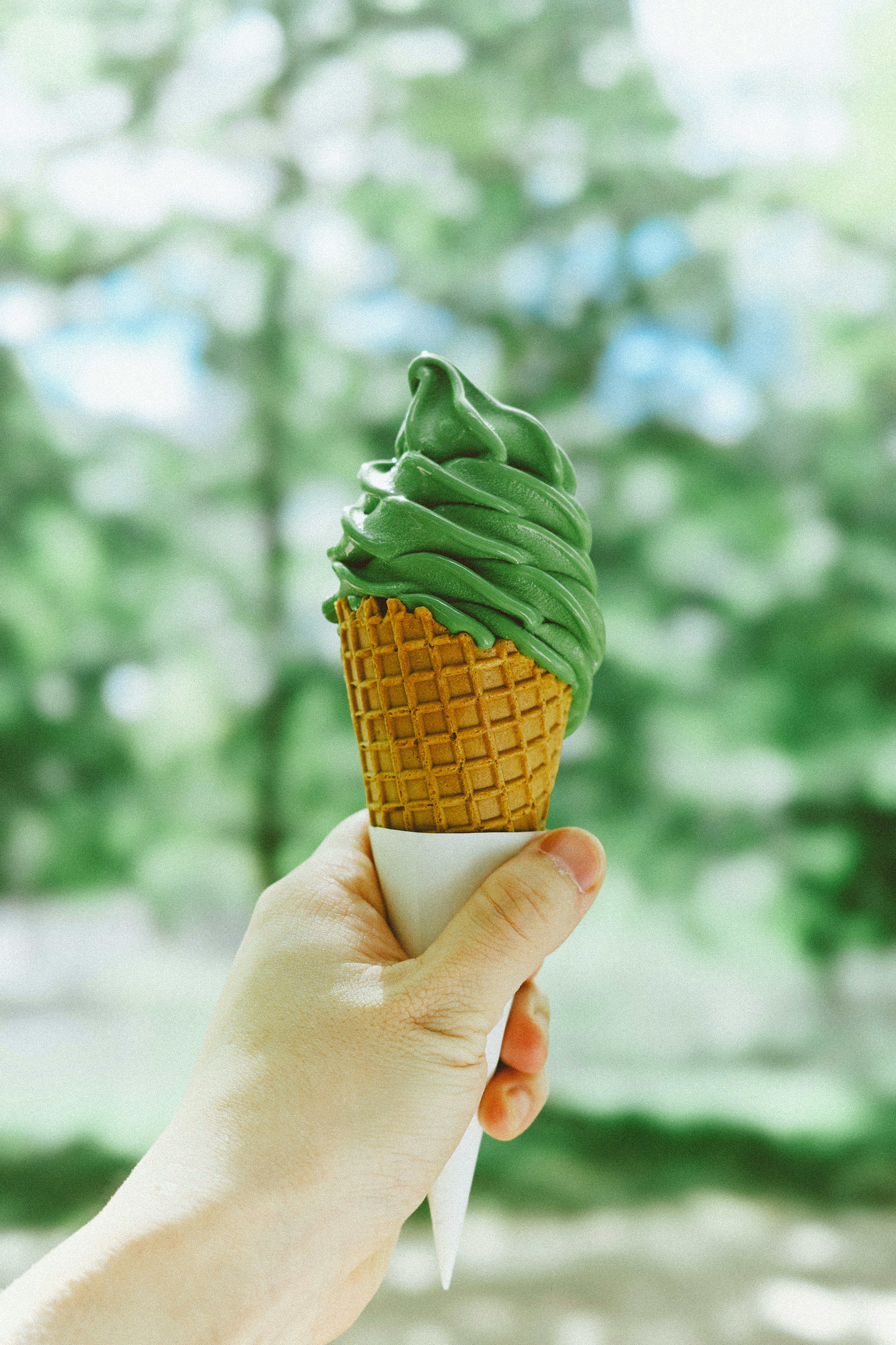 Hand holding green tea soft serve ice cream cone
