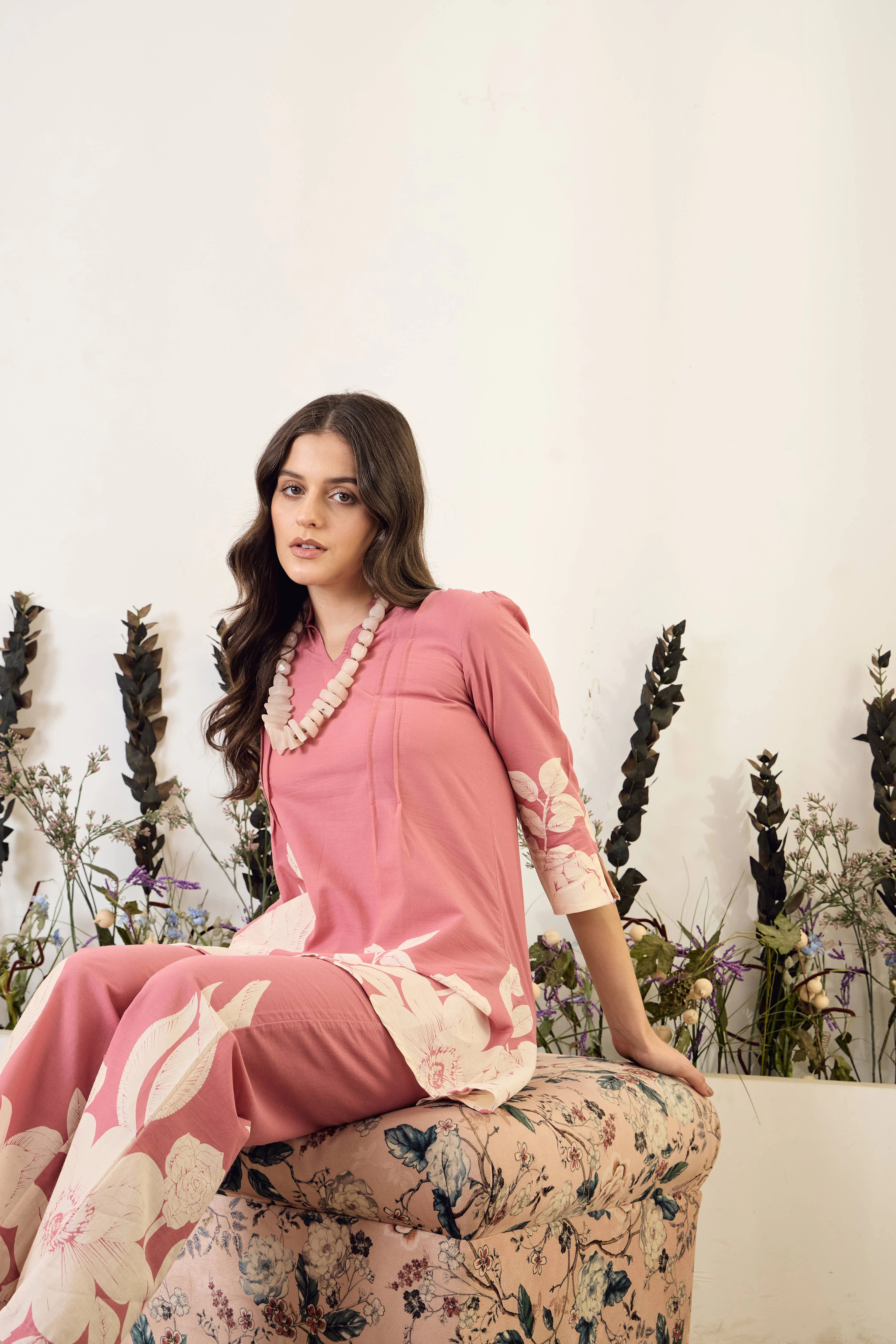 Woman in a rose pink floral kurta set seated on an ottoman