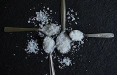 Four spoons filled with salt arranged on a dark surface