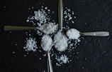 Four spoons filled with salt arranged on a dark surface