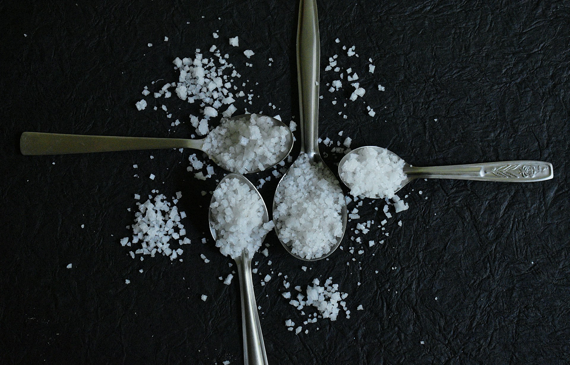 Four spoons filled with salt arranged on a dark surface