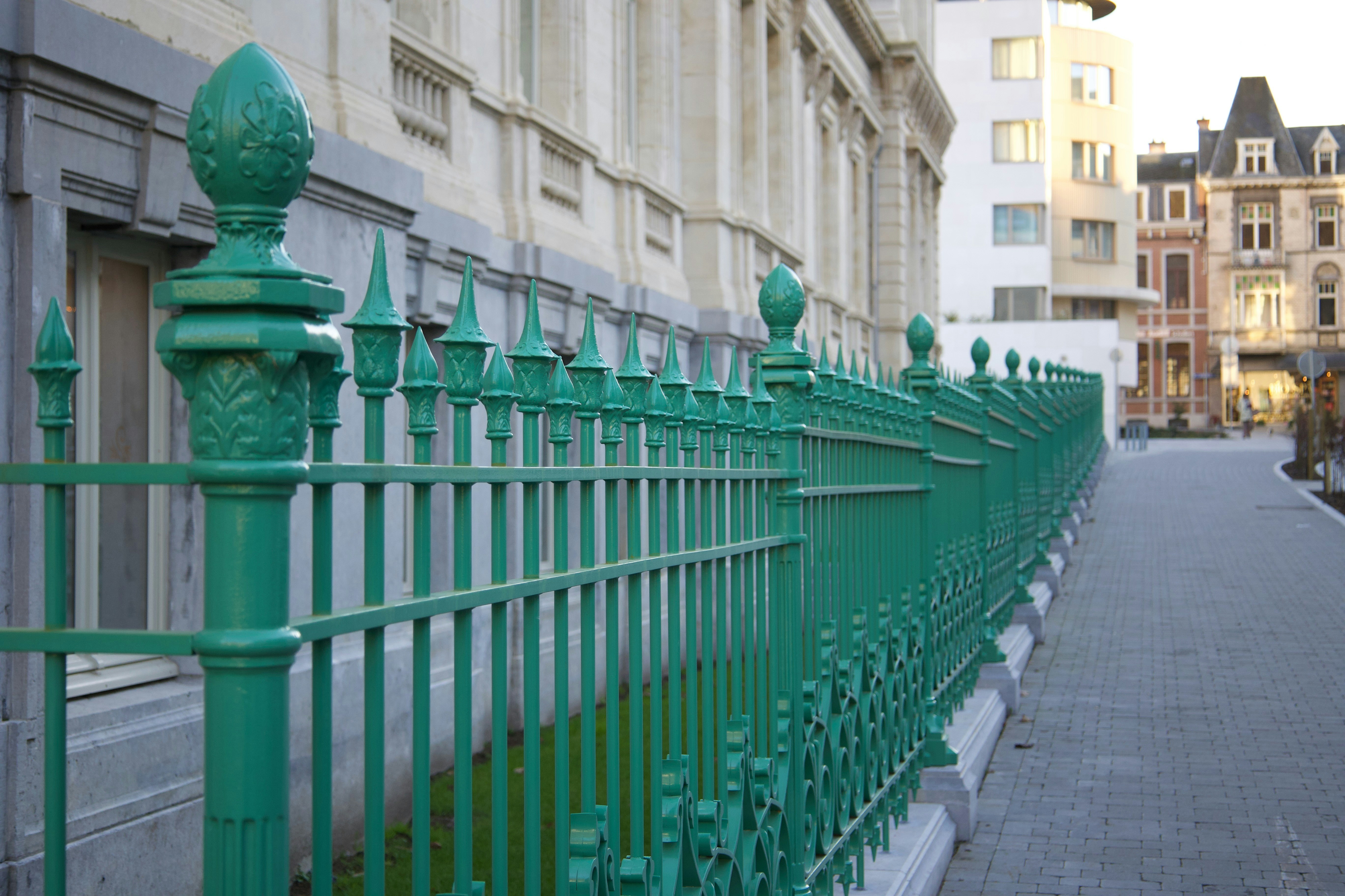 Green ornate fence along a paved walkway