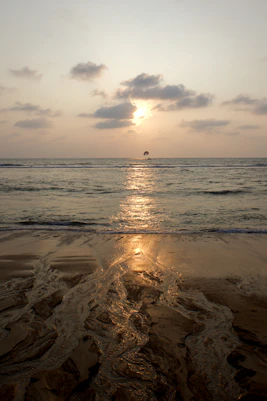 Parasailing over the ocean at sunset with wet sand.