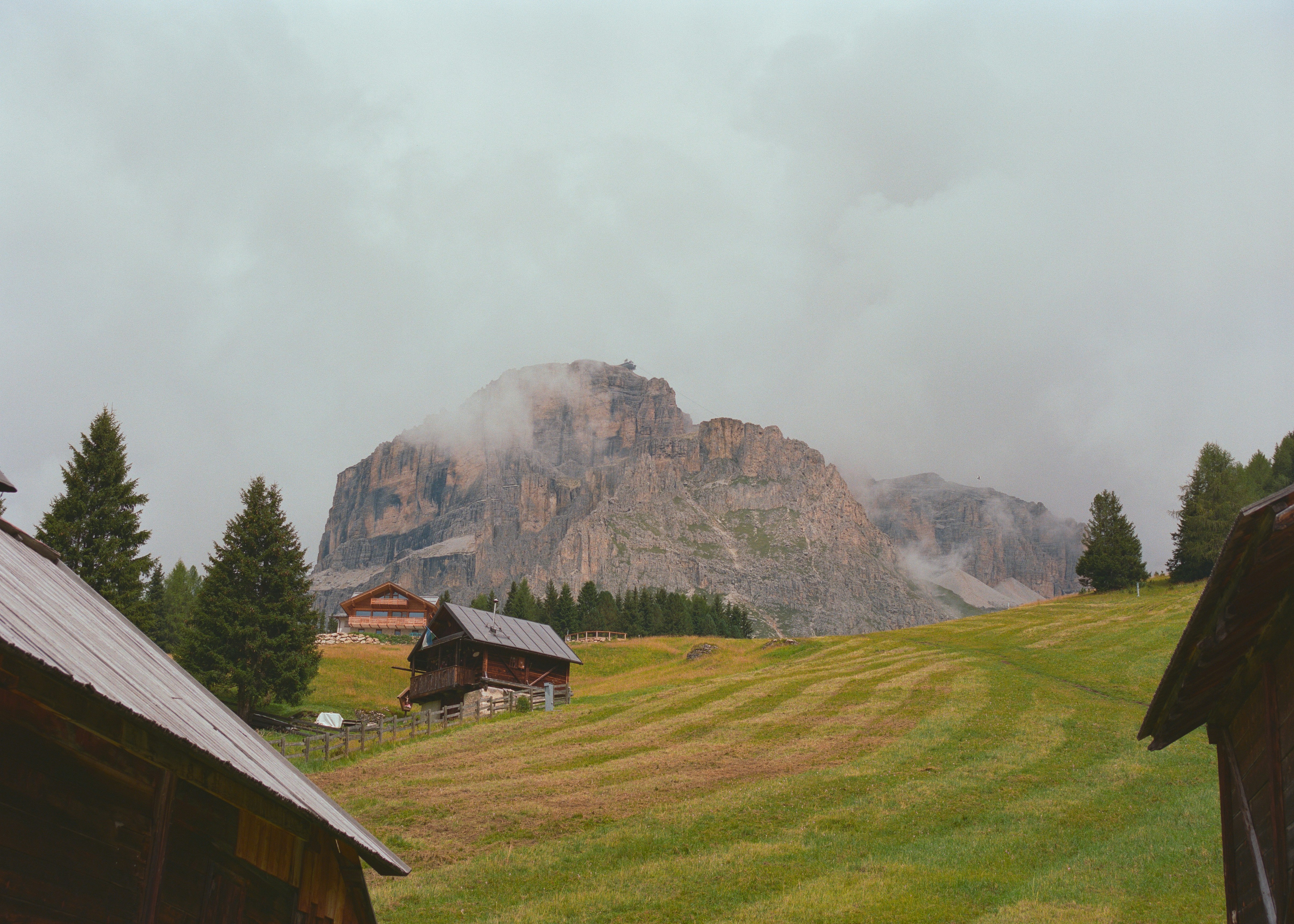 Wooden cabins in a grassy field with mountains.