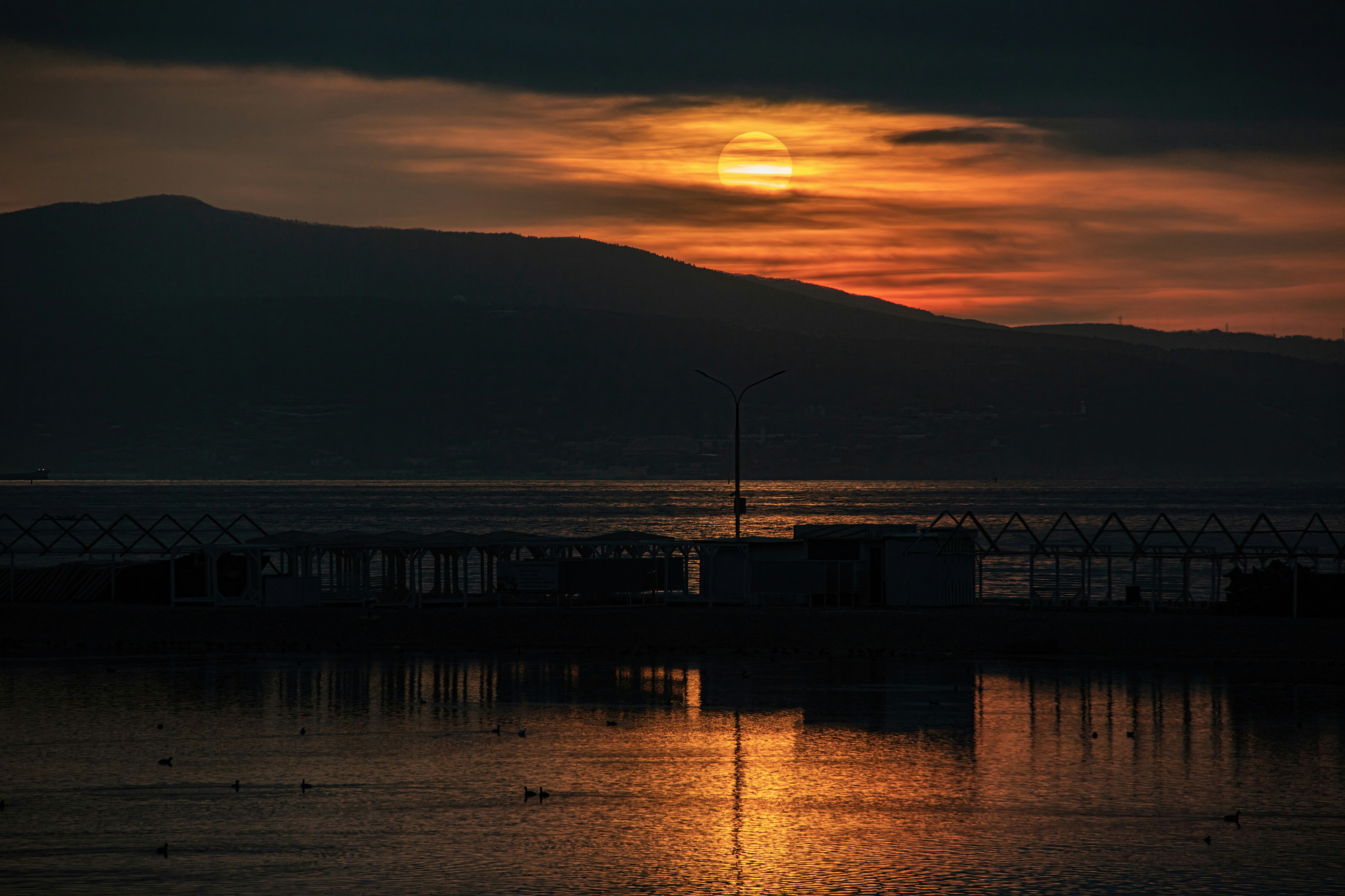 Coucher de soleil sur un lac calme avec des montagnes lointaines.
