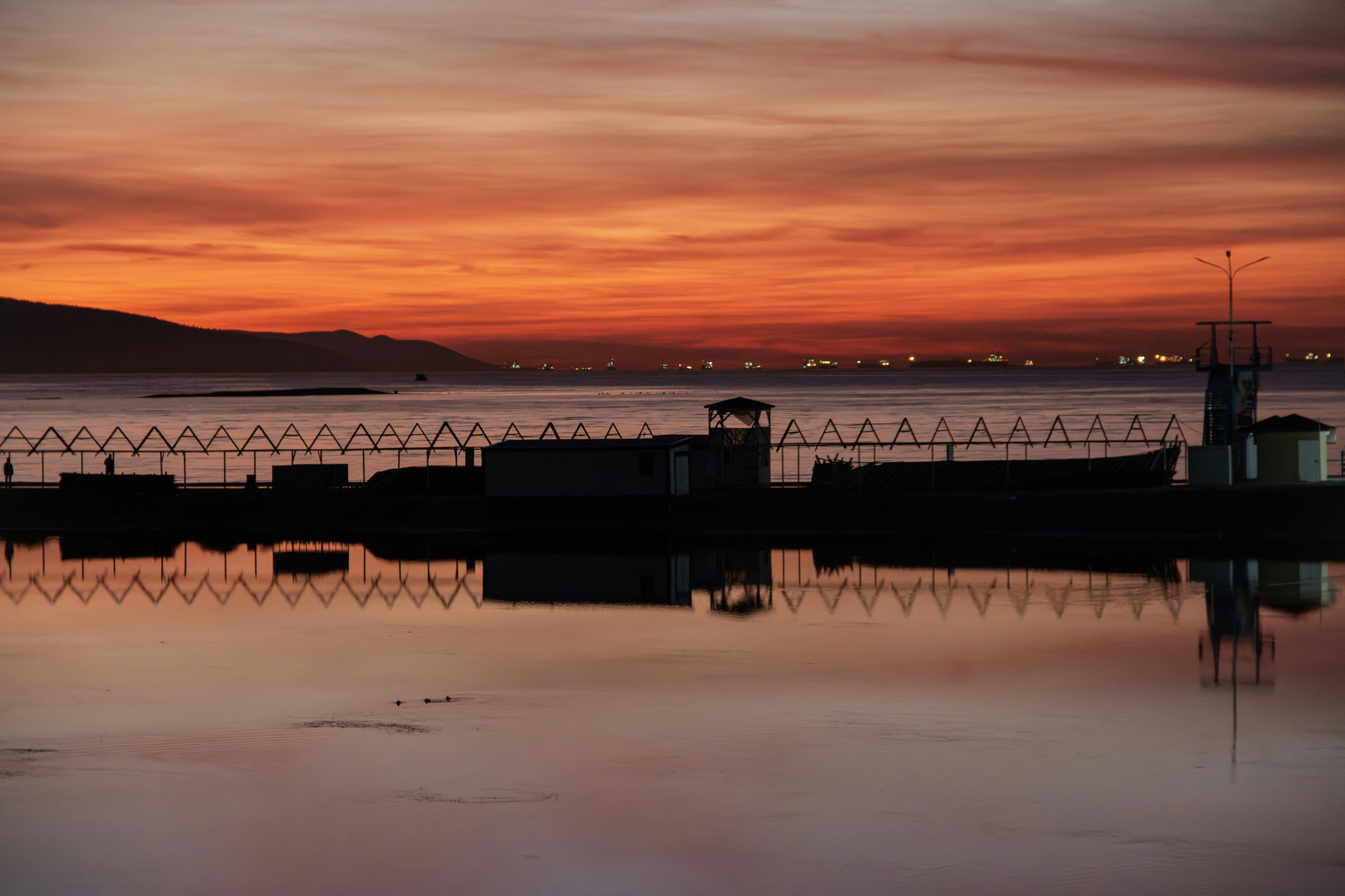 Coucher de soleil sur une baie calme avec des lumières lointaines.