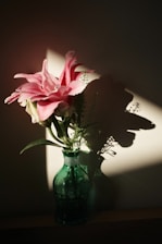 Pink lilies in a green vase with dramatic lighting.