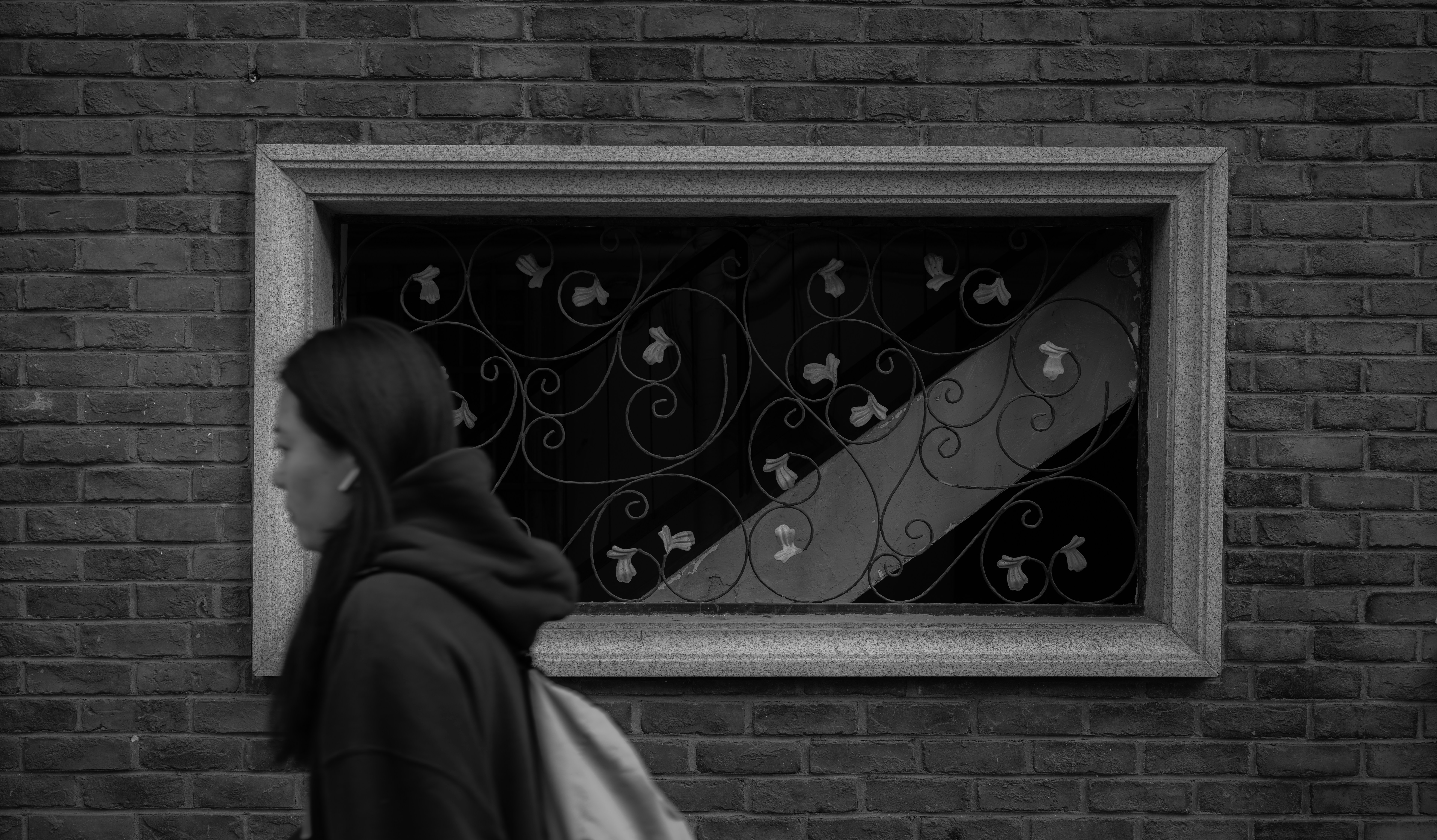 Une femme passe devant une fenêtre décorative sur un mur de briques