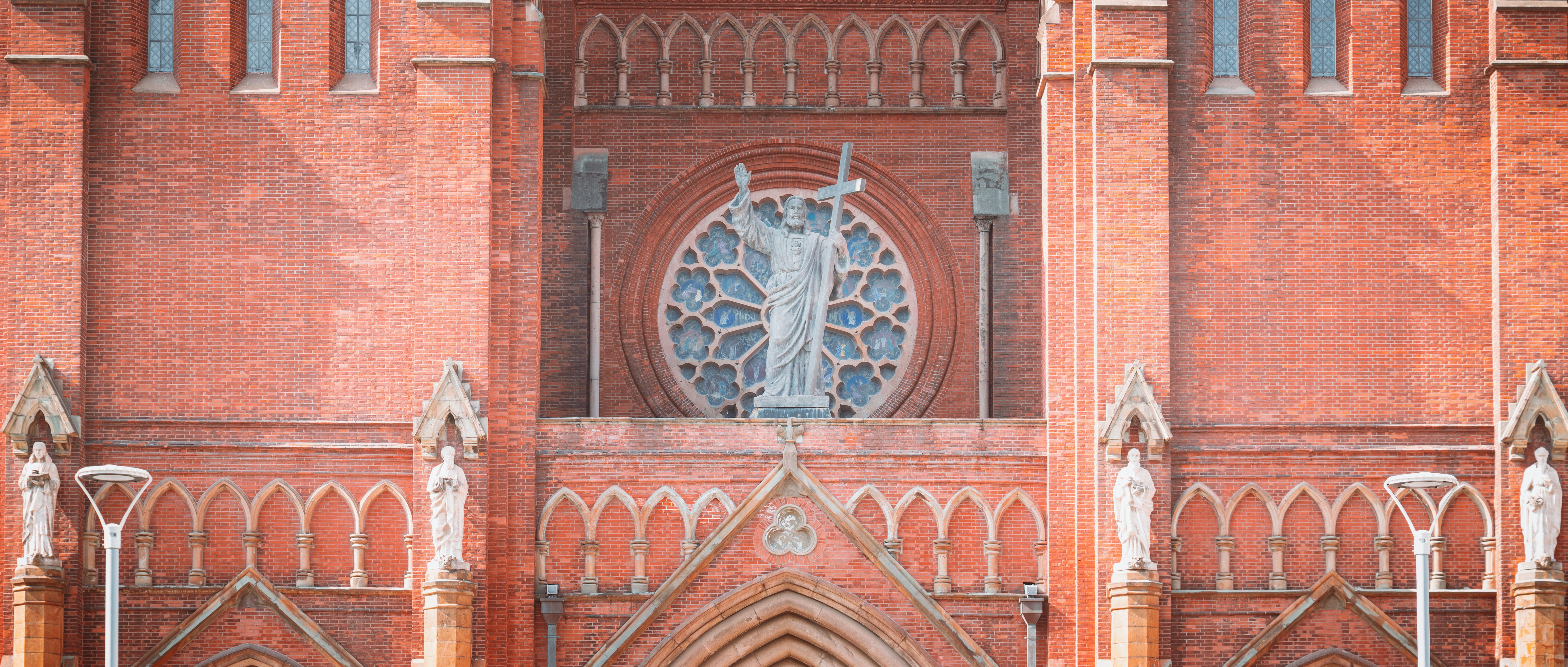Façade ornée d’église en brique rouge avec vitraux.