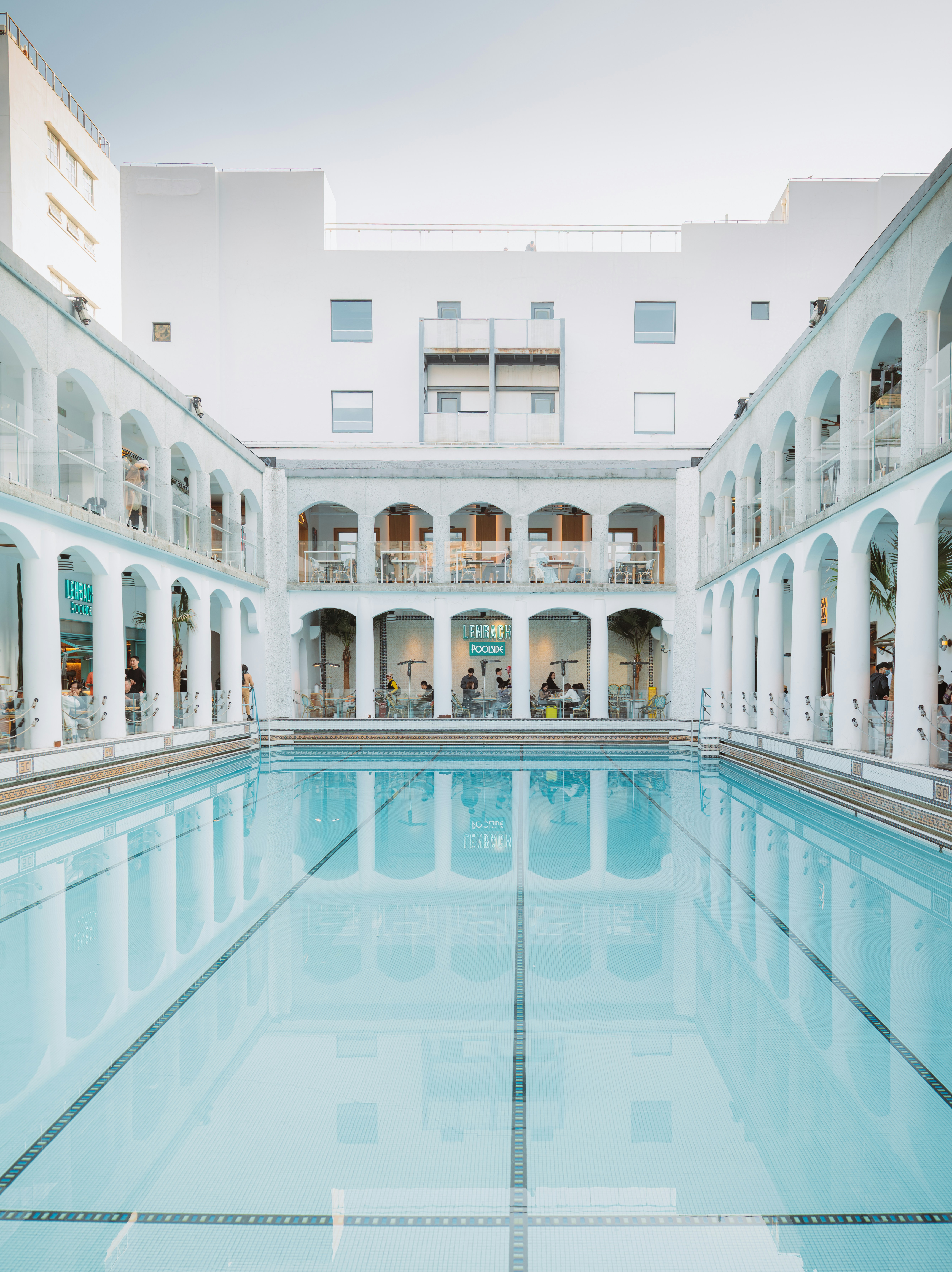 Piscine élégante avec colonnades blanches et bâtiment moderne.
