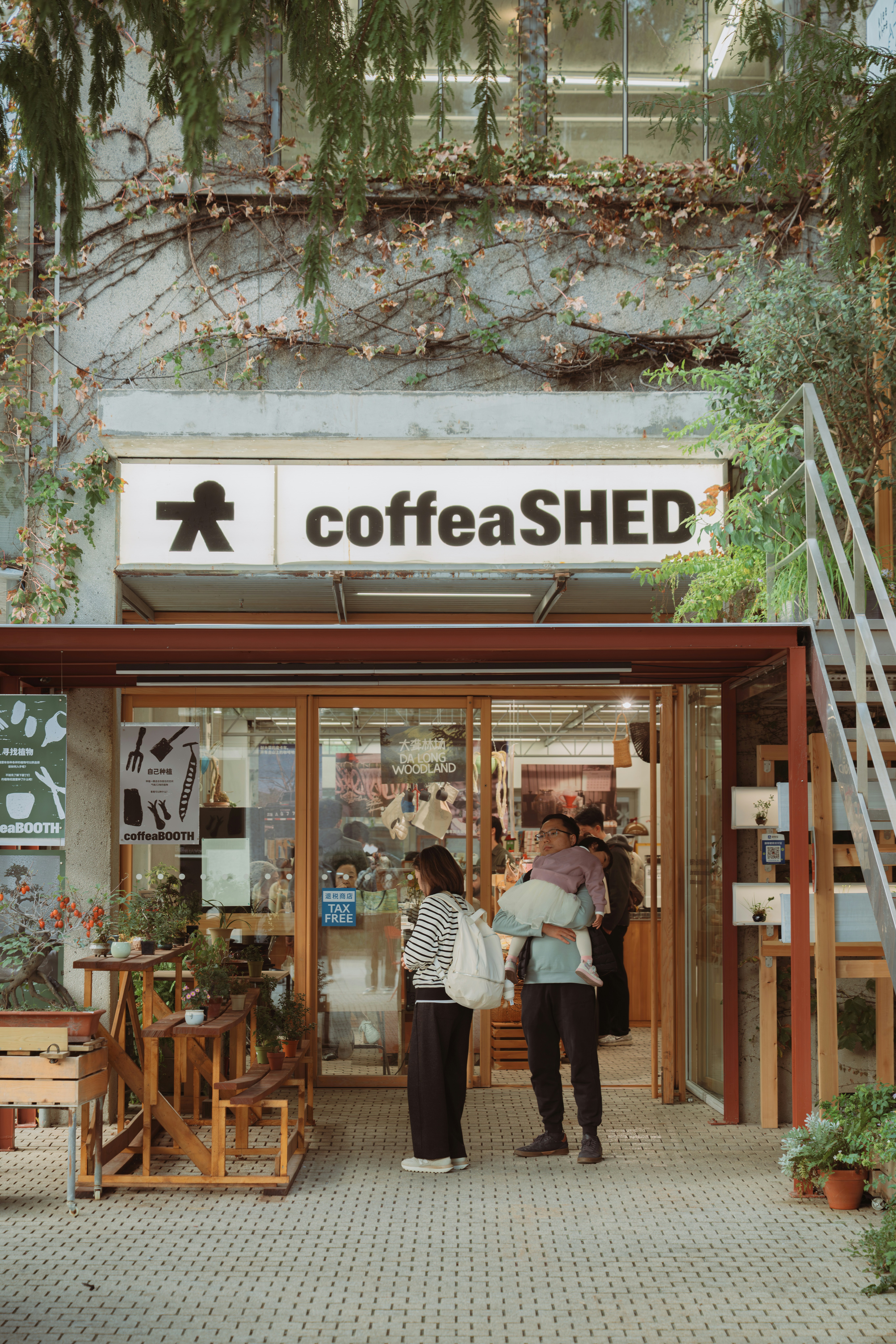 Des gens entrant dans un café avec des plantes dehors.