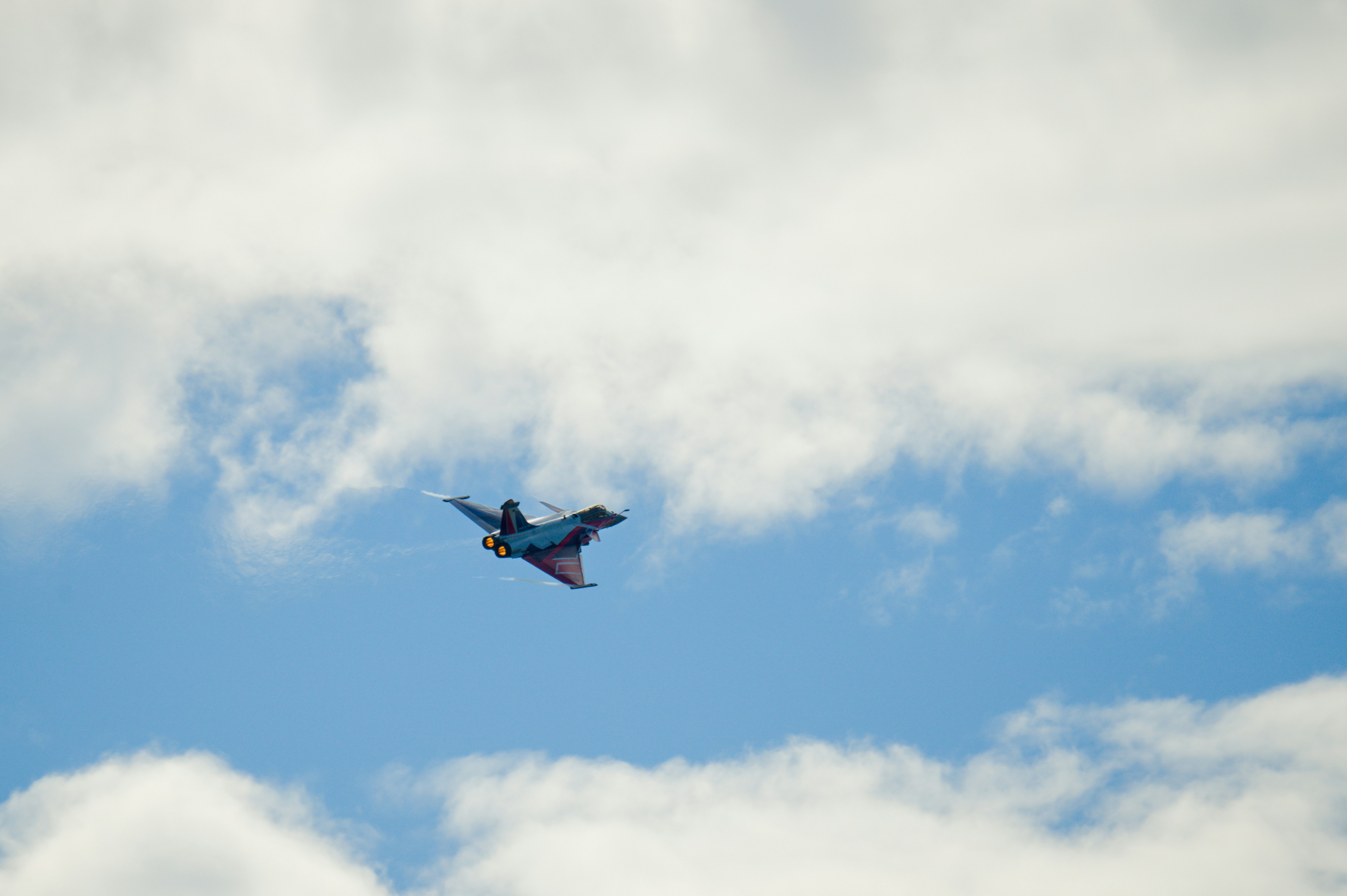 A fighter jet flies through a cloudy blue sky.