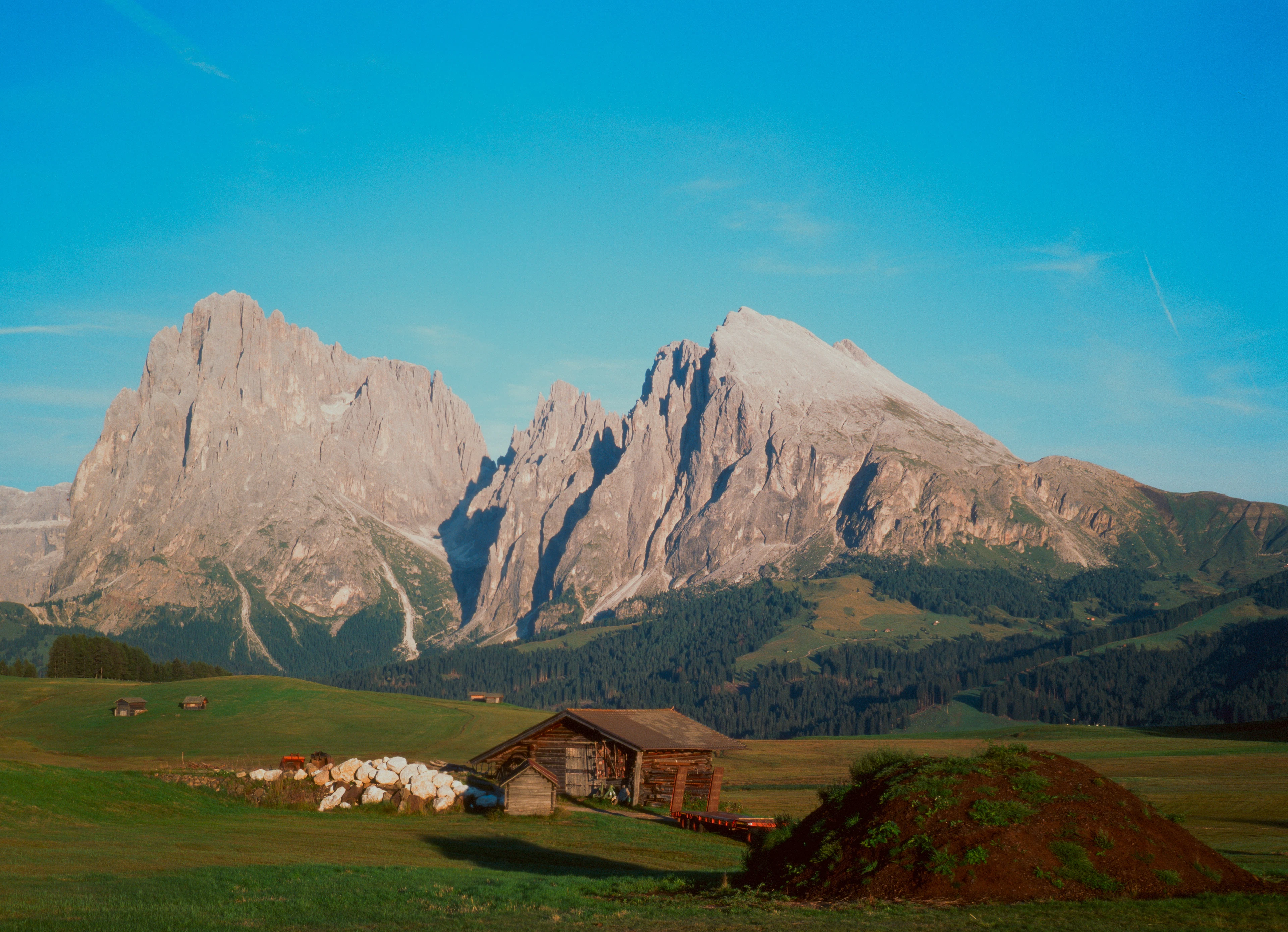 A wooden hut in a green meadow on the Alpe di Siusi beneath the mountain walls in morning light