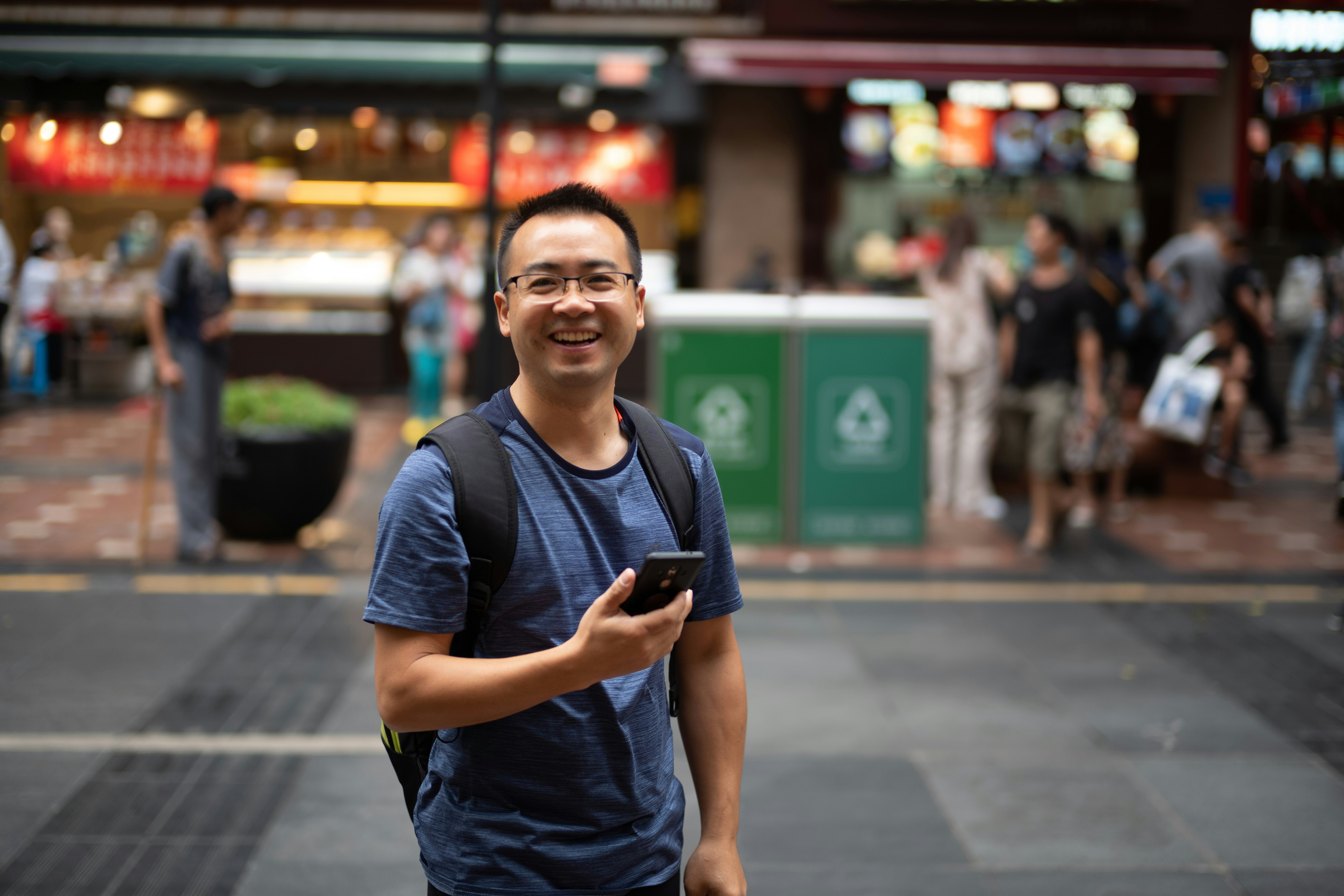 Smiling man holding a smartphone on a city street.