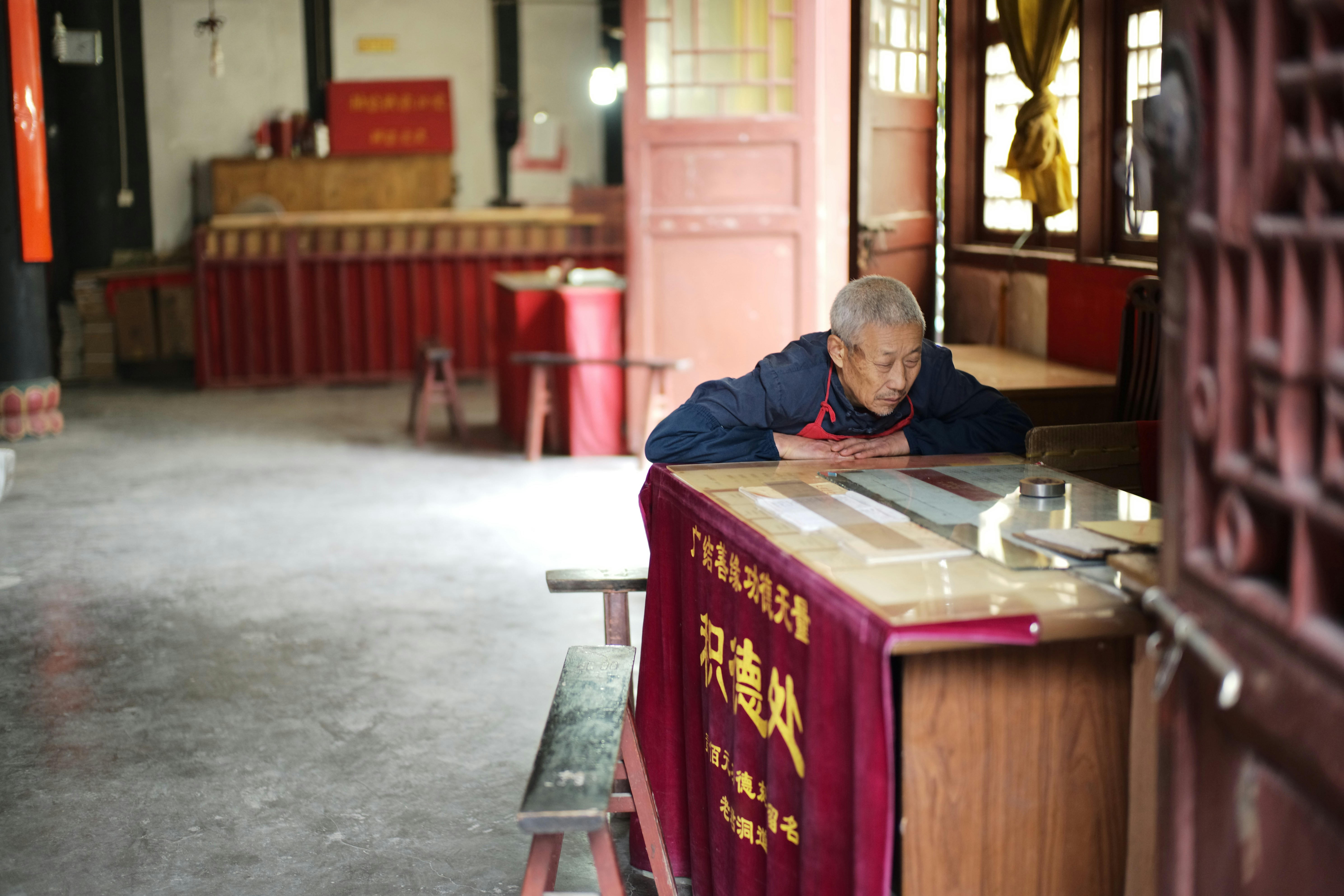 Elderly man leaning on a counter in a building.
