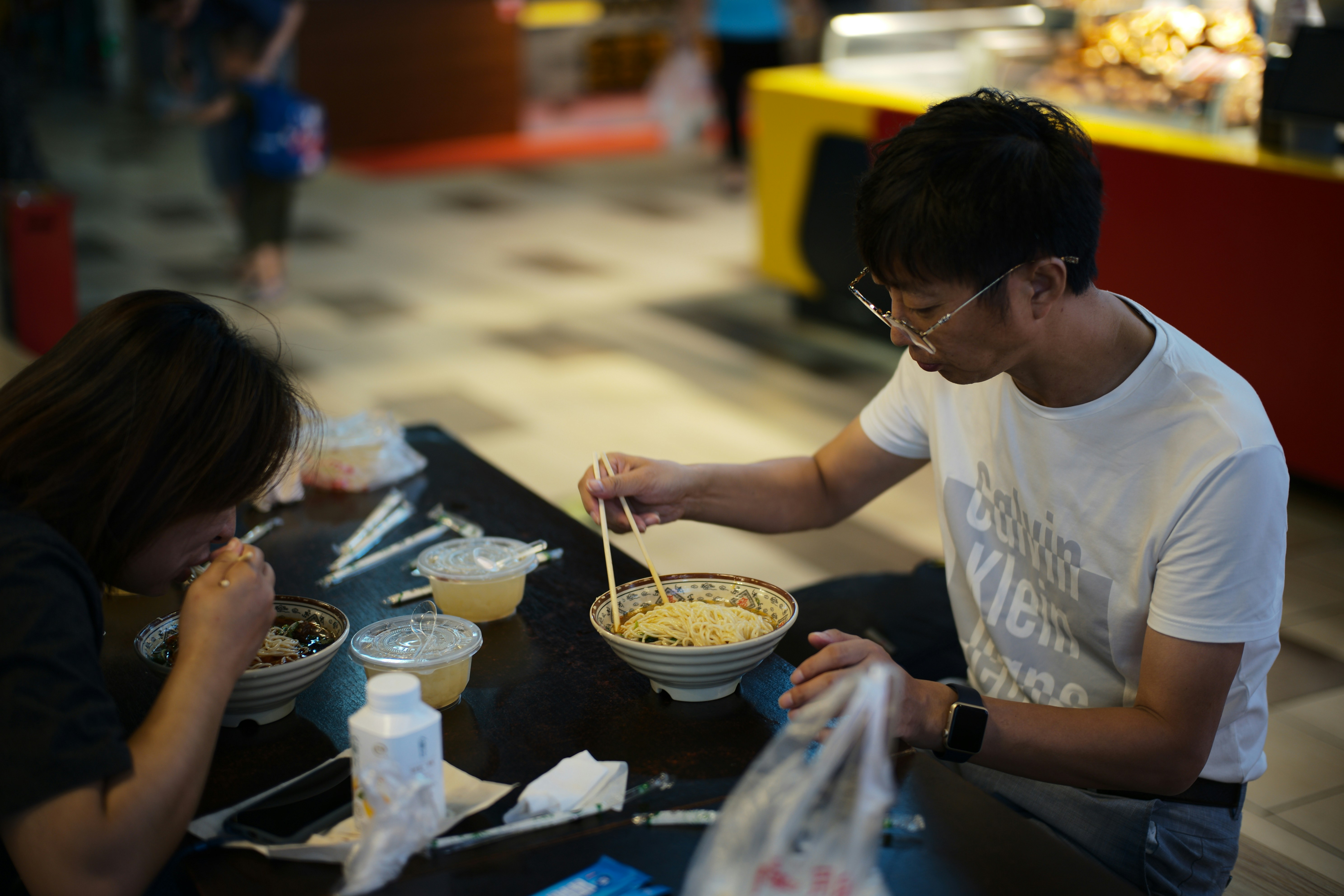 Two people eating noodles at a table.