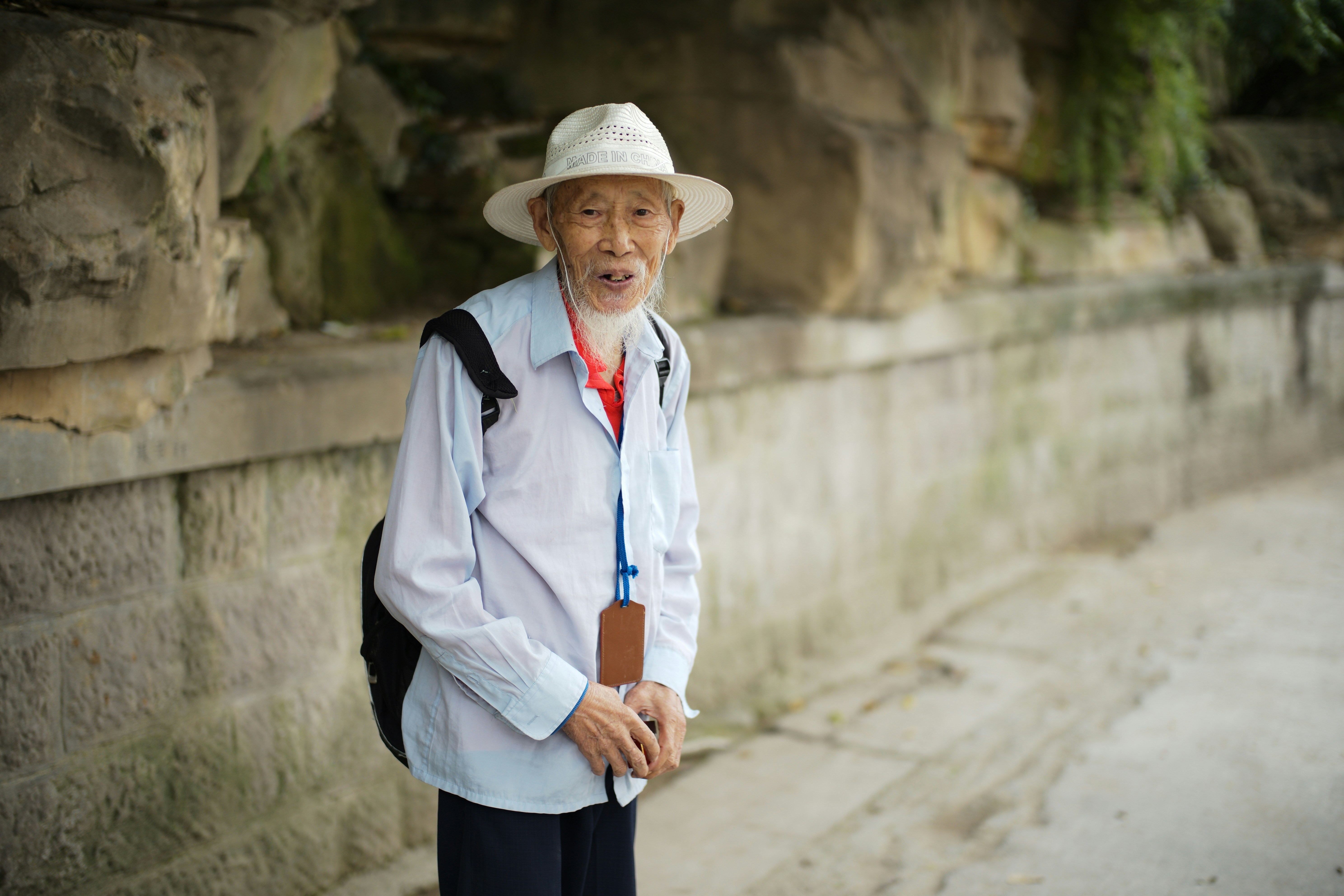An elderly man in a hat stands outdoors.