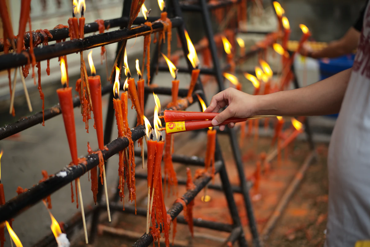 Hands lighting candles at a Thai temple for Makha Bucha