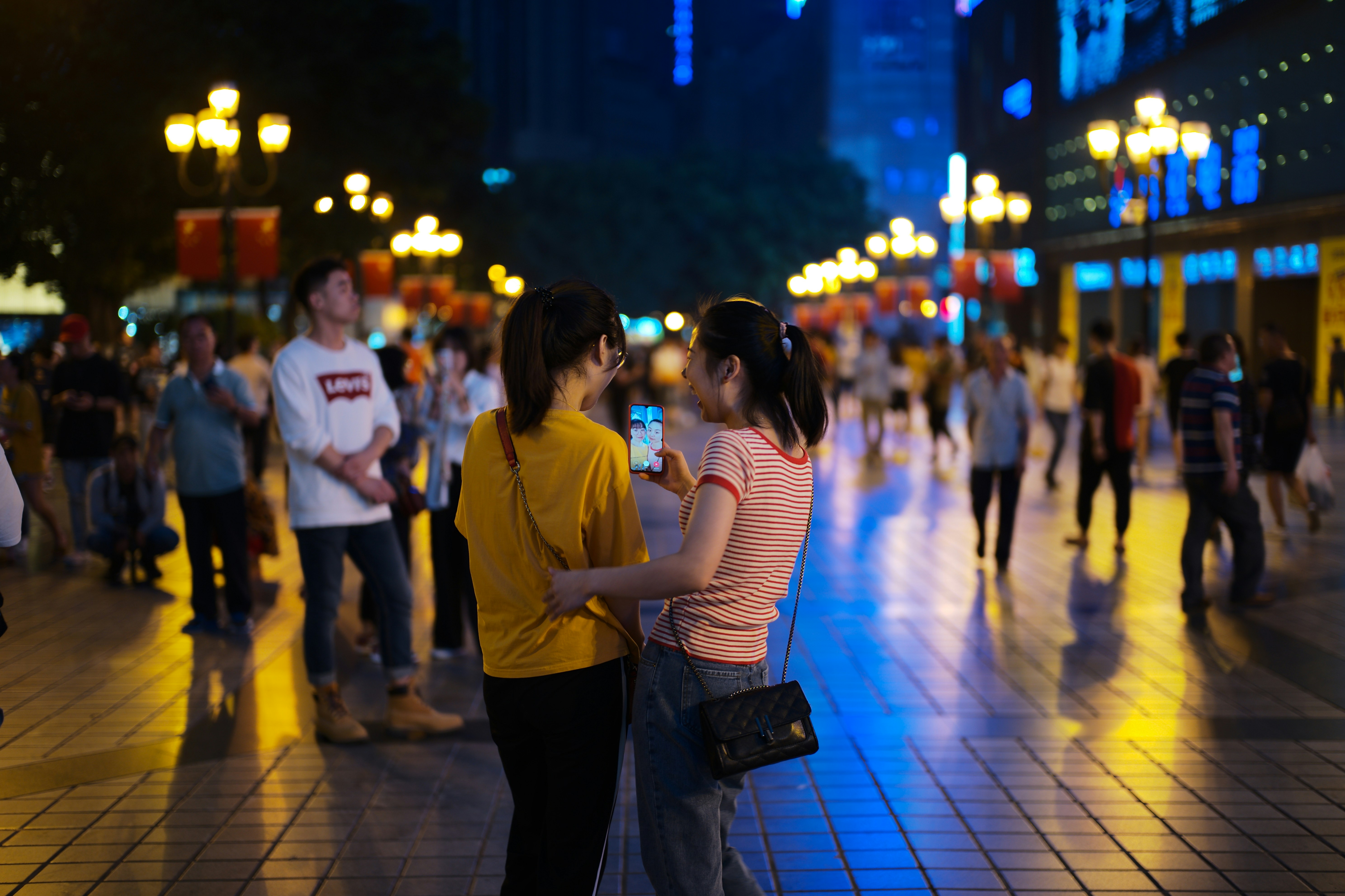 People looking at a phone in a city at night
