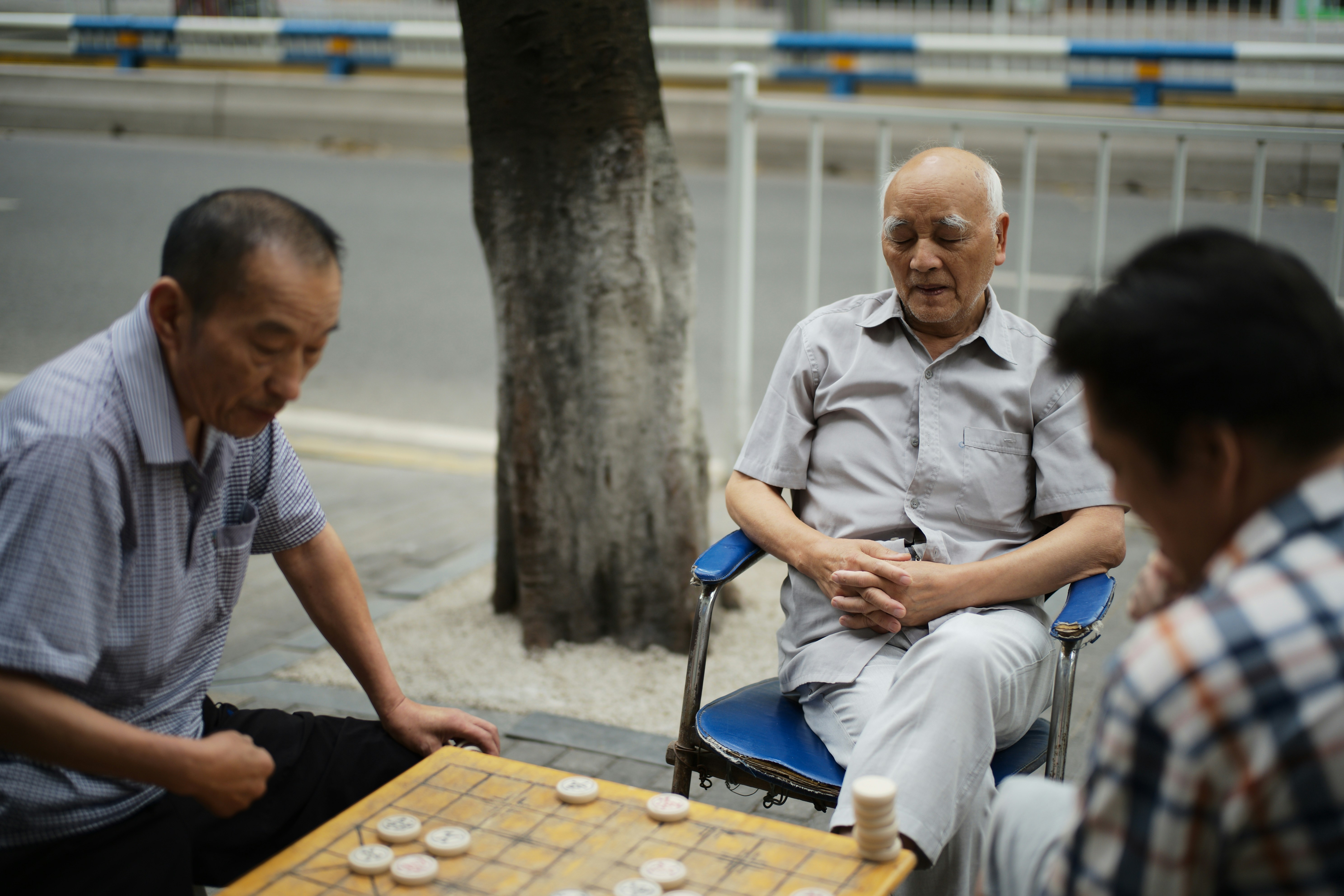Three elderly men playing a board game outdoors.