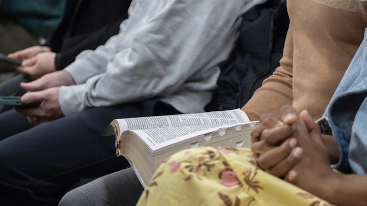 Hands folded beside an open Bible in a group setting