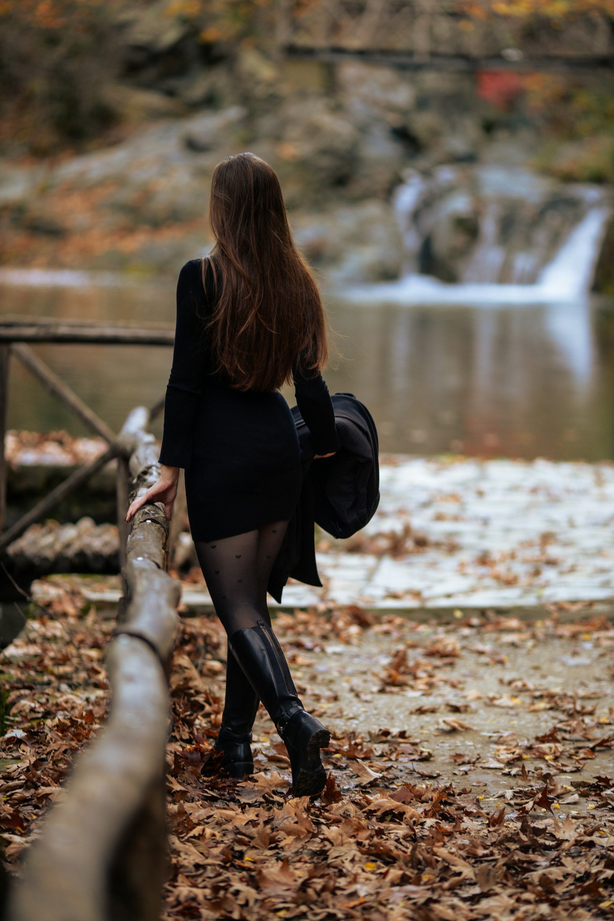 Woman in black dress walks by autumn waterfall