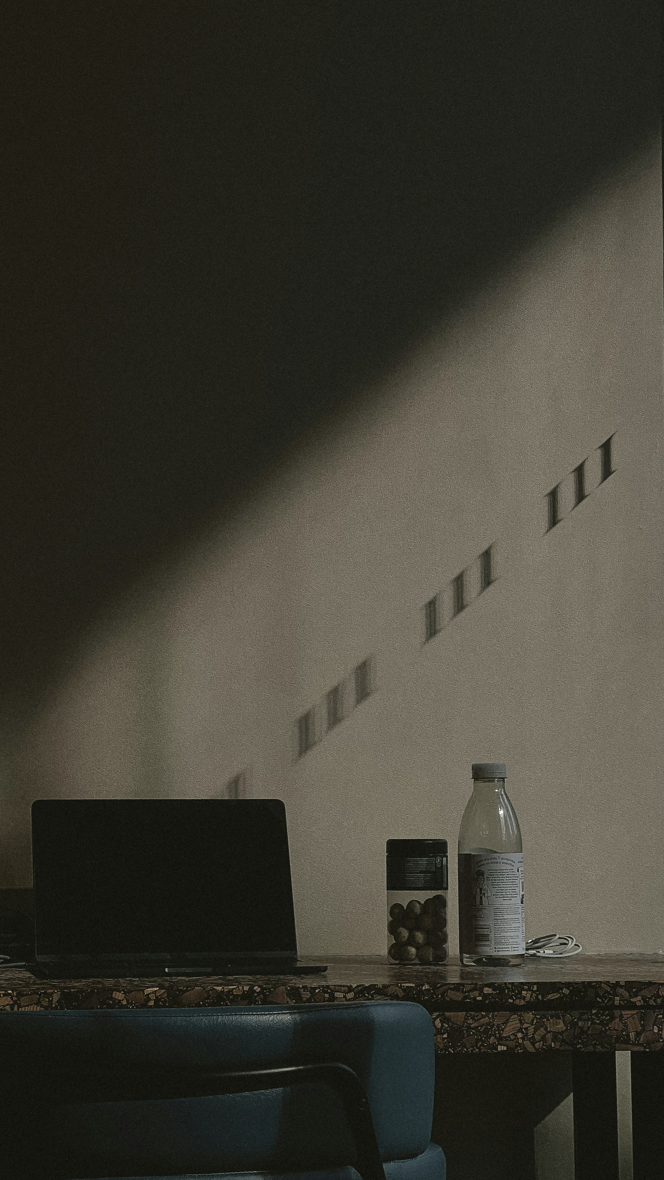 Laptop, water bottle, and jar on desk with sunlight shadows.
