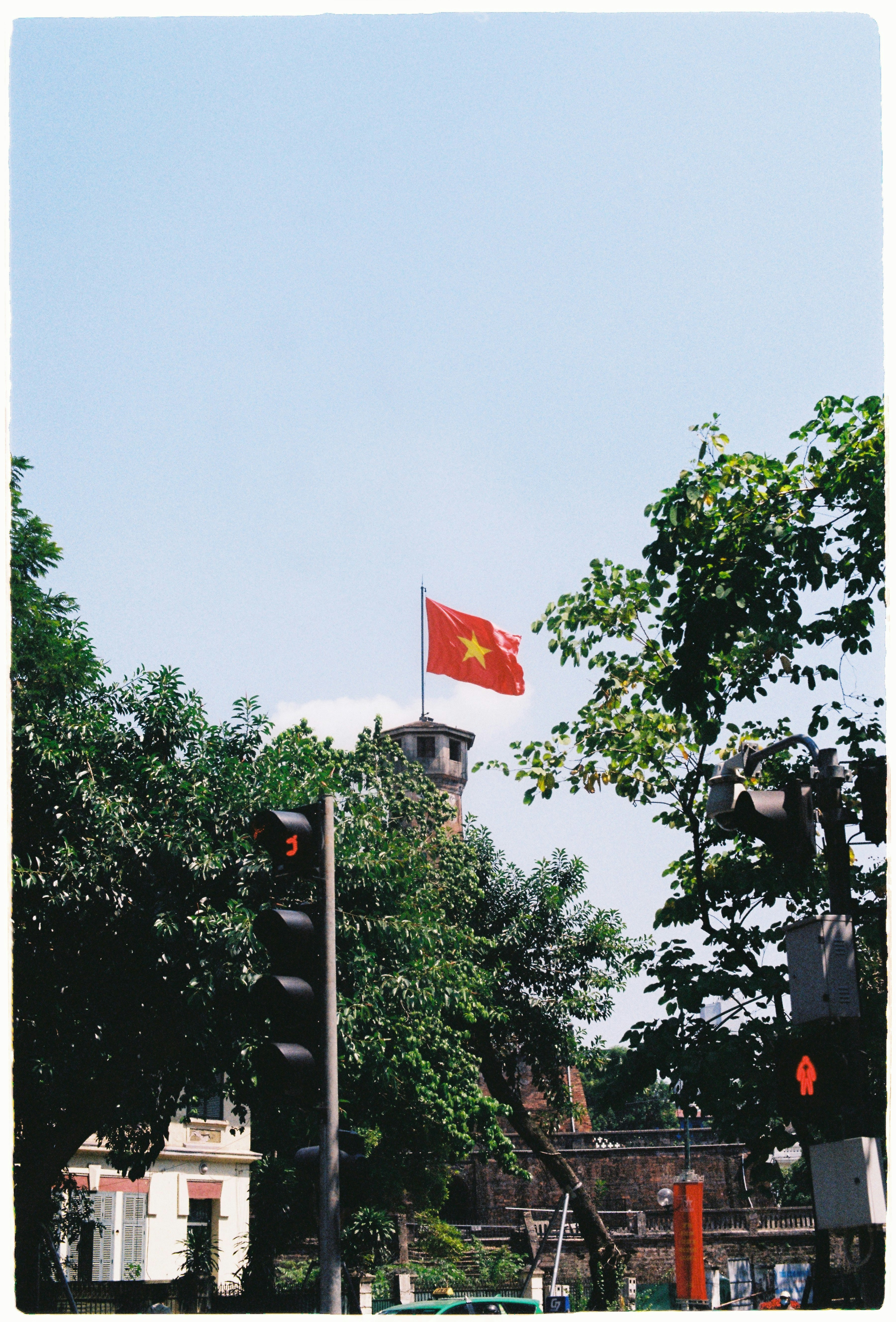 Vietnamese flag flying above a tower with trees.