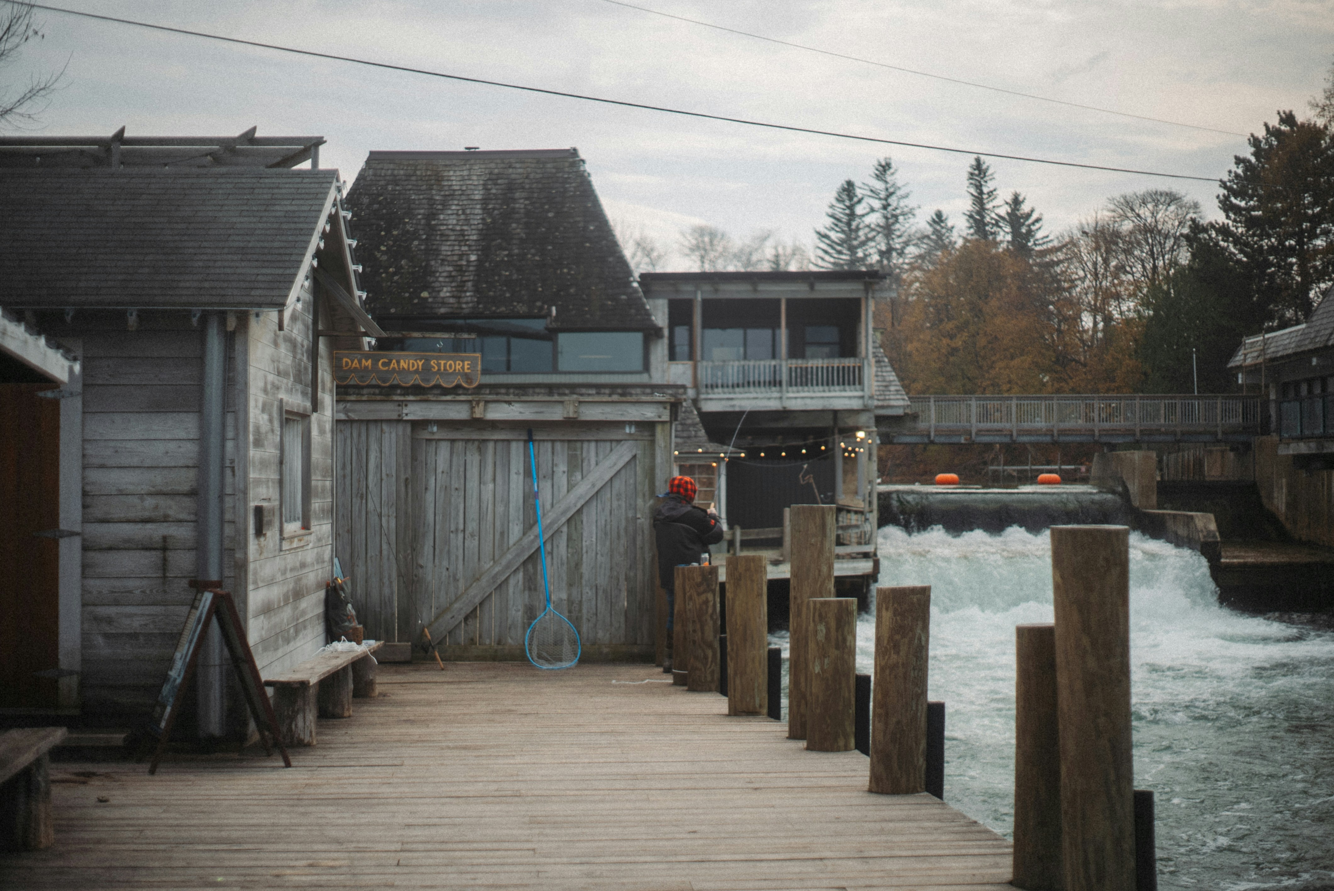 Wooden buildings beside a flowing river with a bridge.