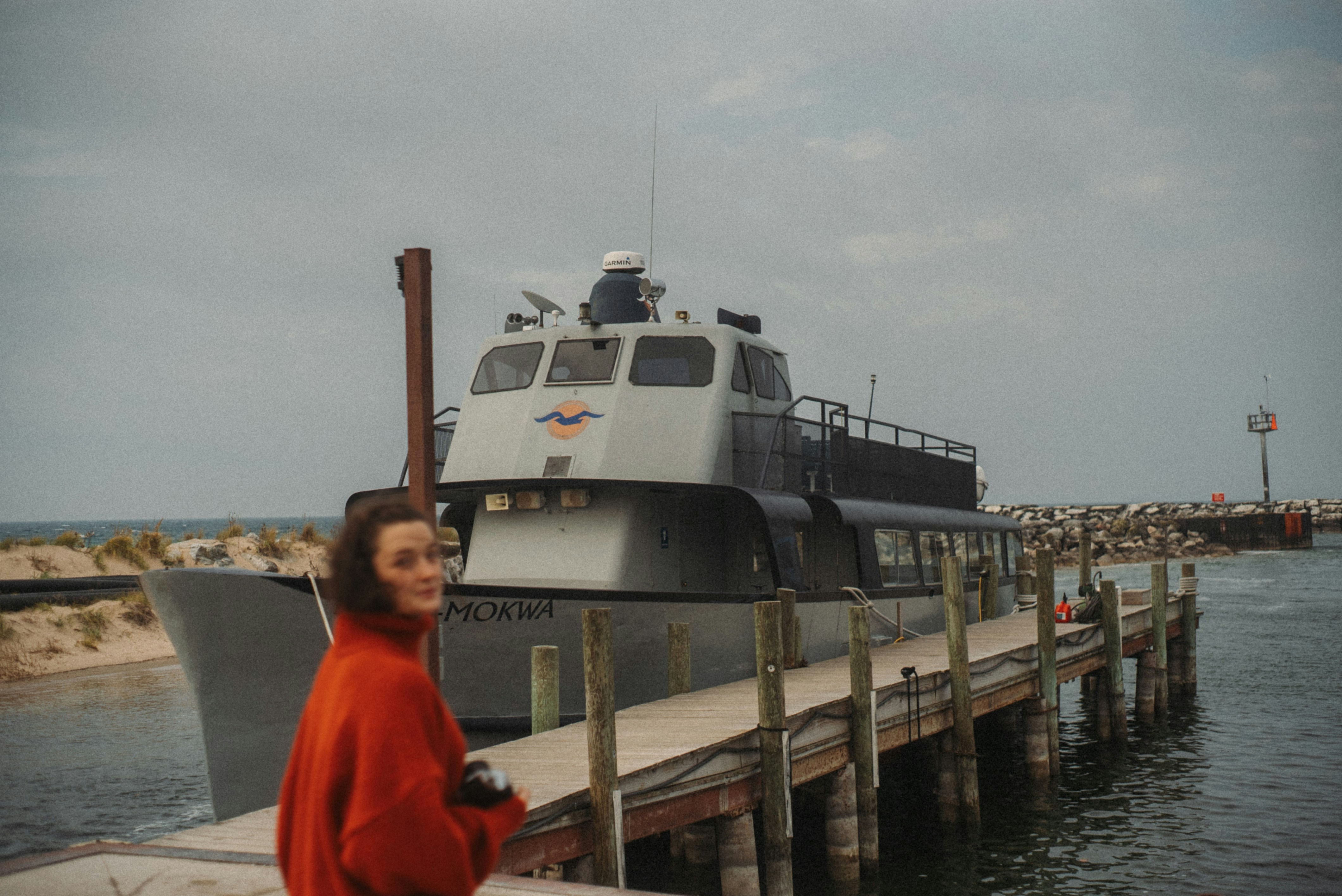 Woman with camera stands by a boat at a dock.