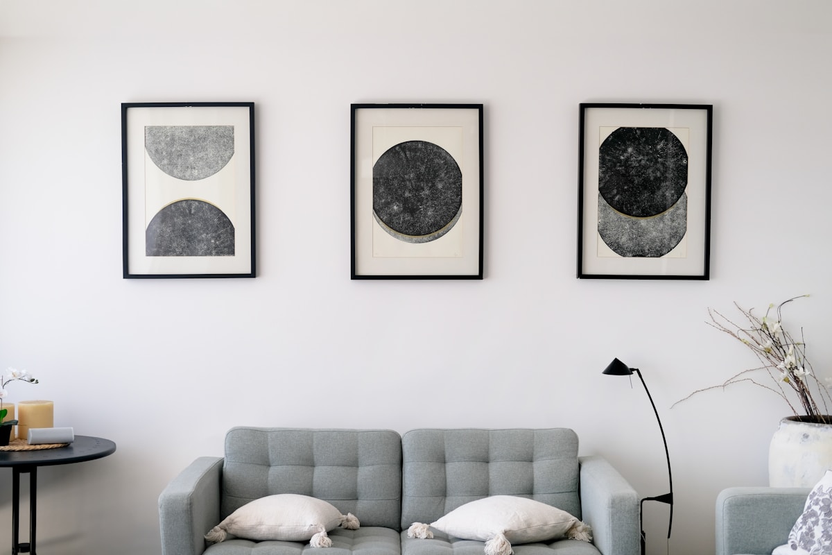 three abstract art prints in black frames above gray sofa apartment wall
