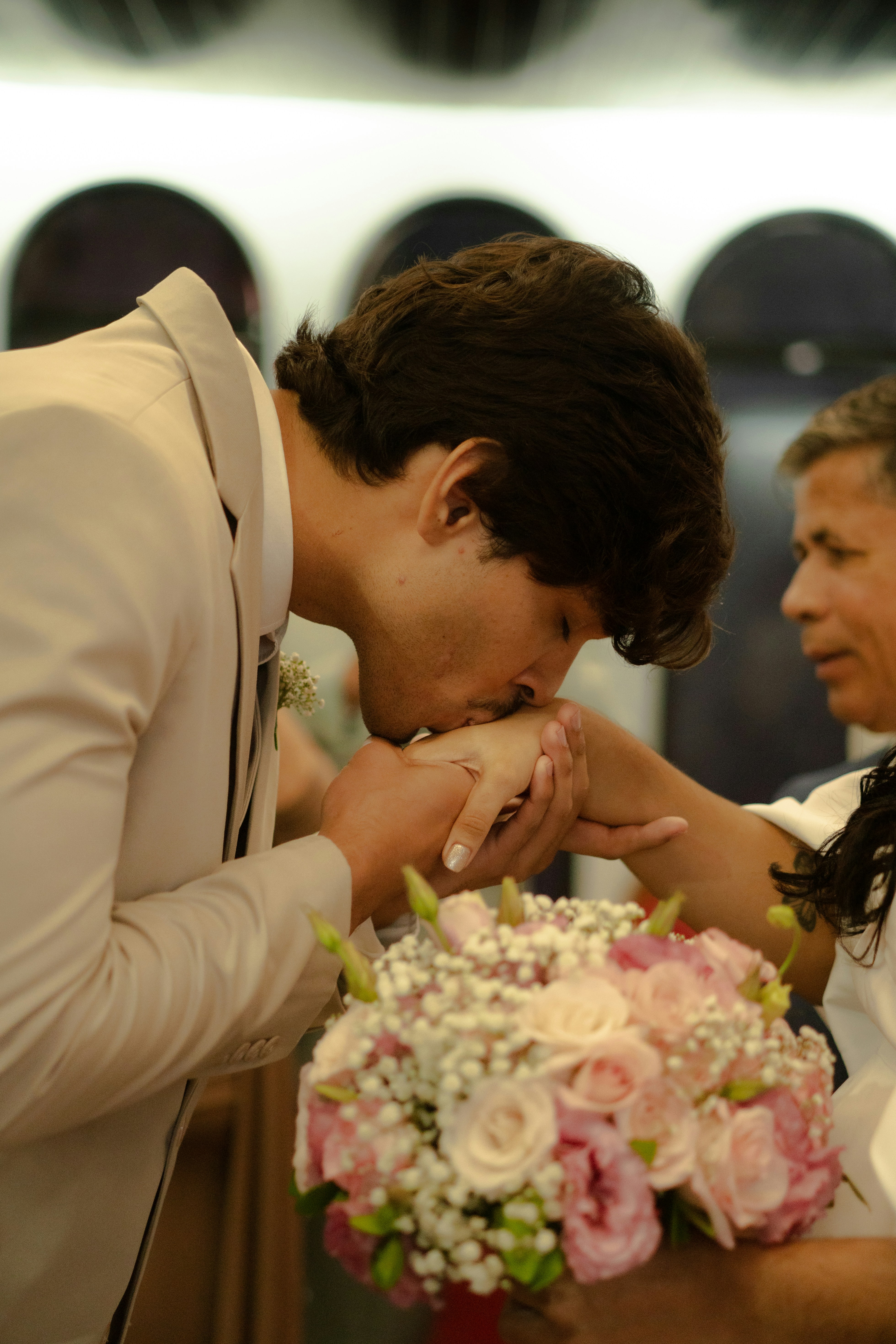 Groom kissing bride's hand with wedding bouquet