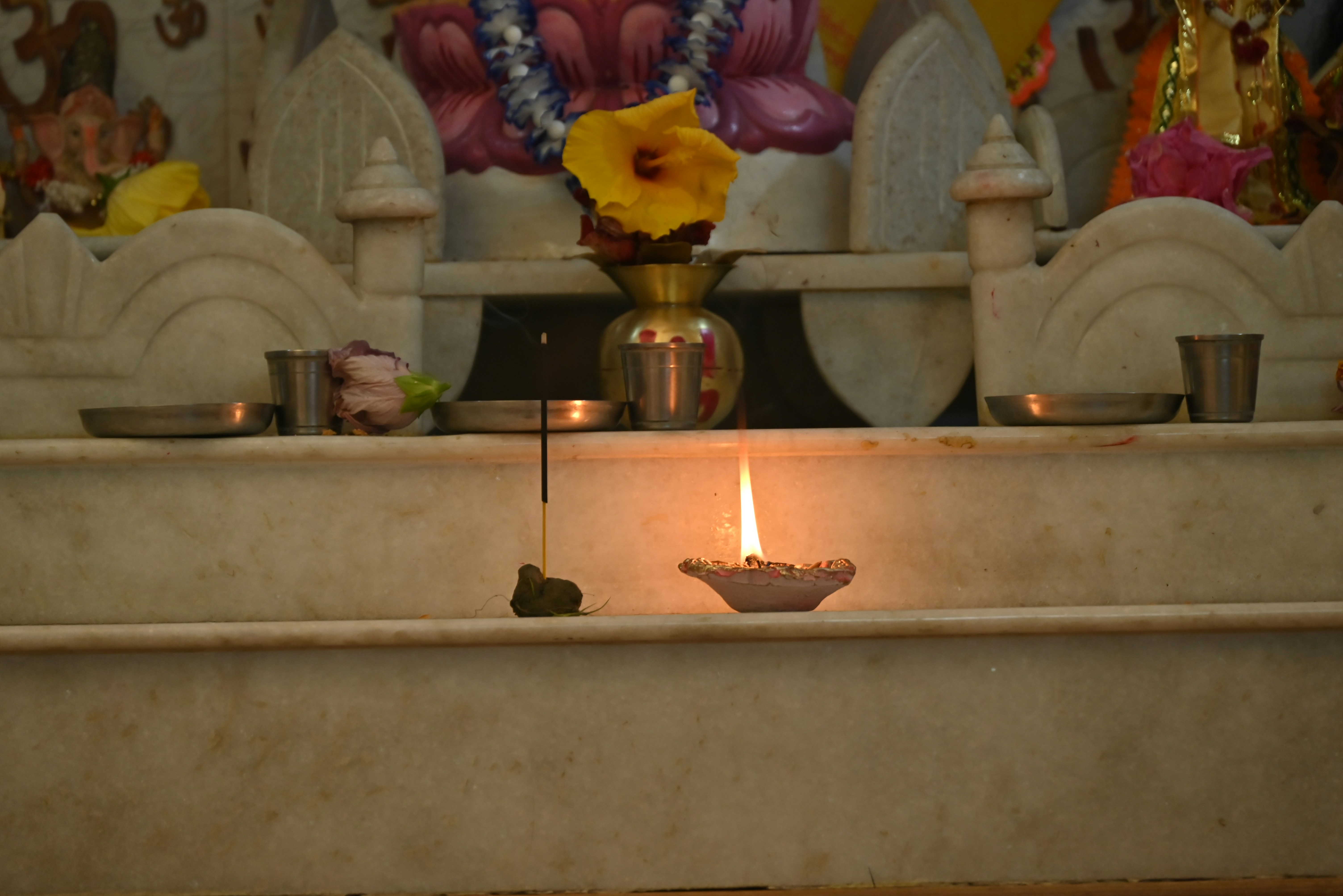 A lit diya with an incense stick and flower.