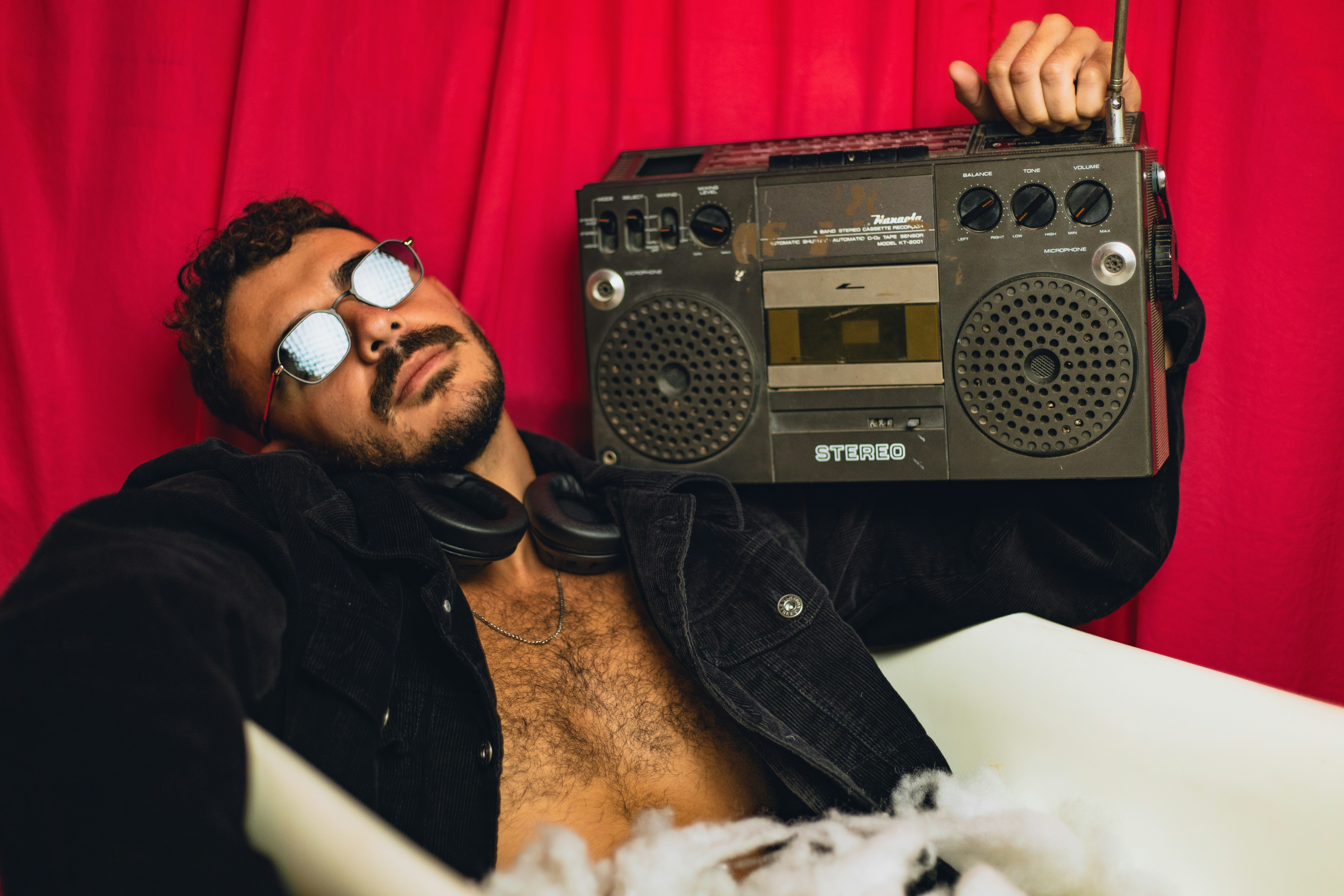 Man holding a vintage boombox with headphones around neck.