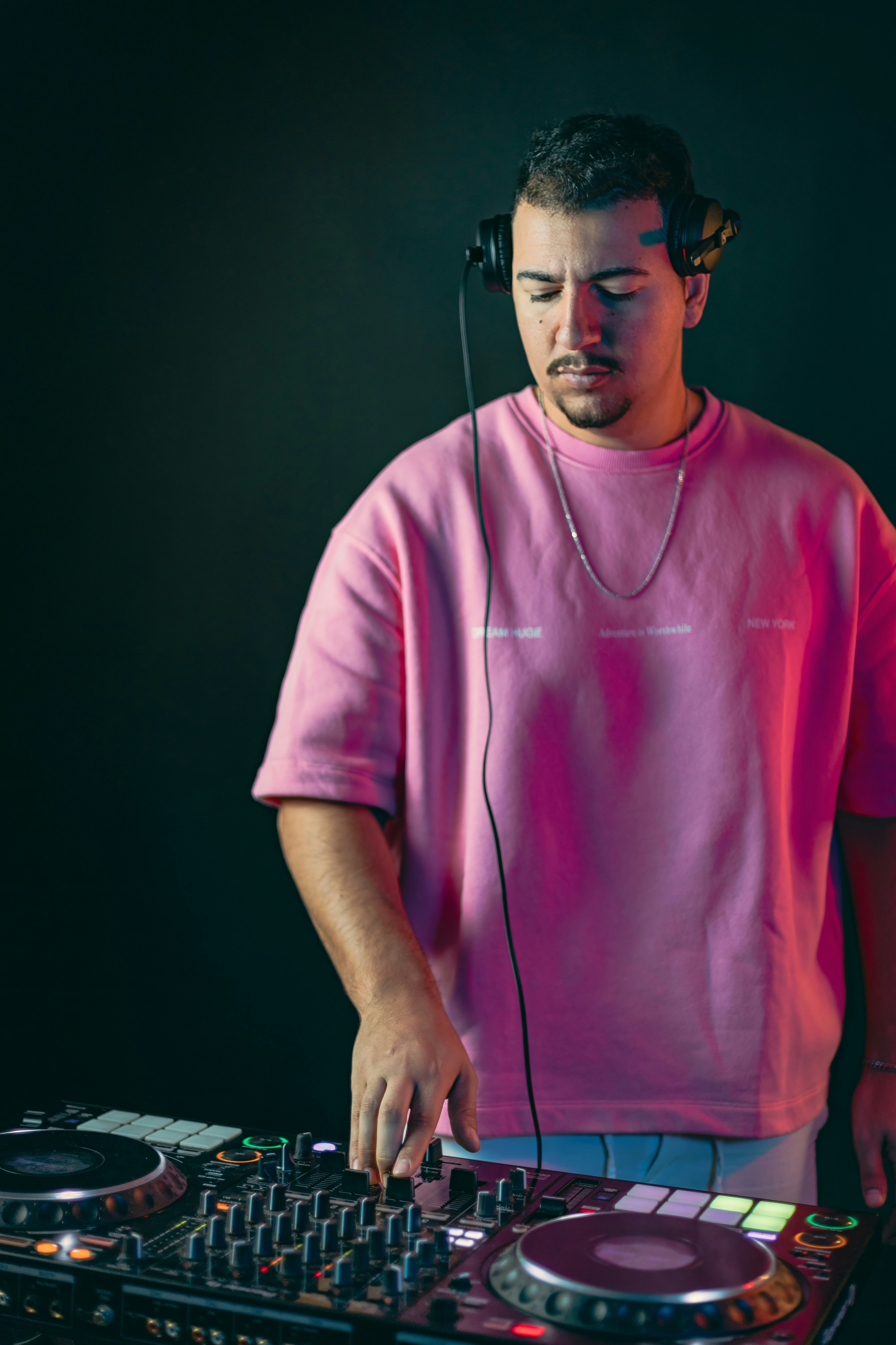 Dj wearing headphones and pink shirt mixing music.