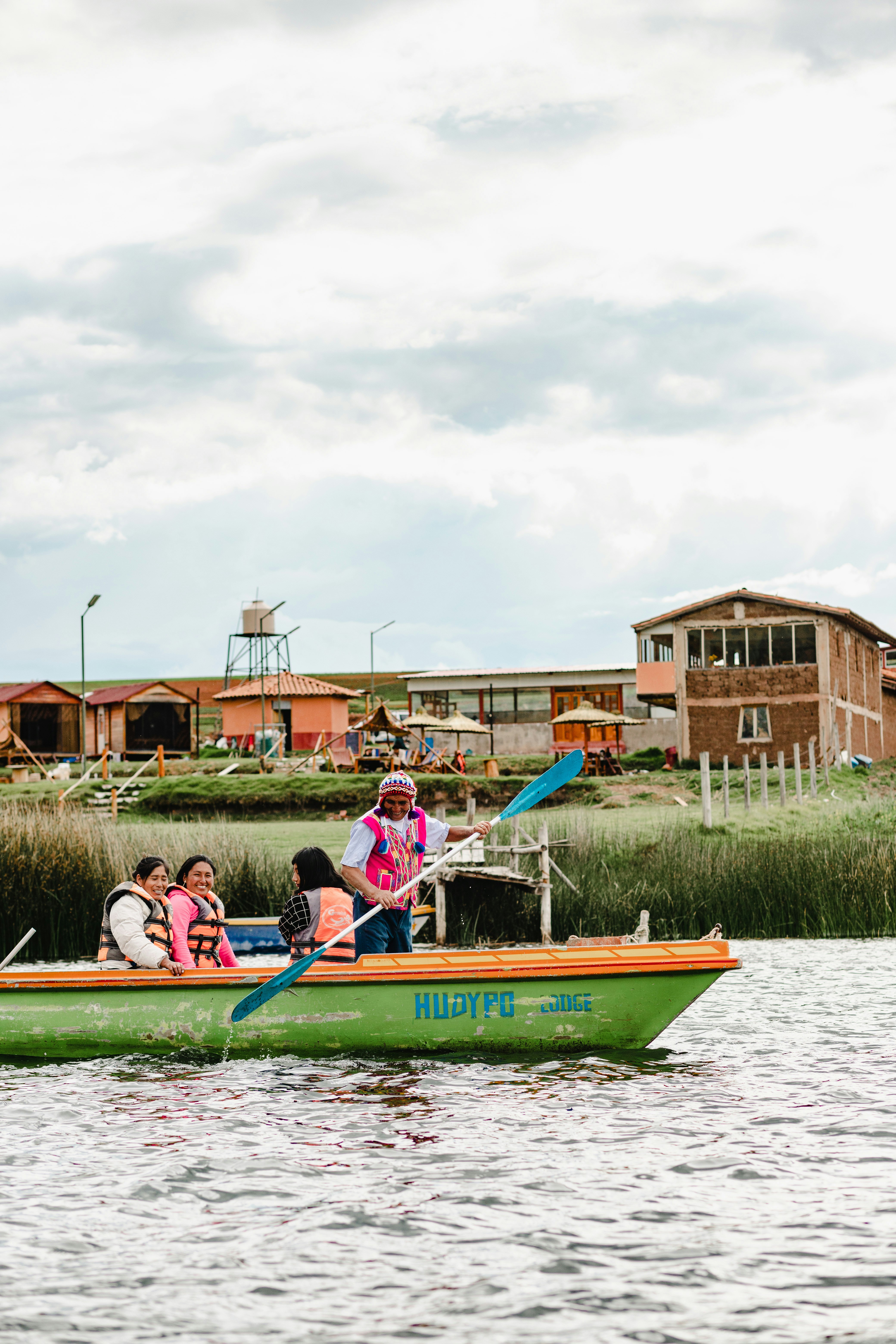 People in a boat on a lake with buildings behind.