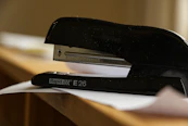 A black stapler rests on a desk with papers.