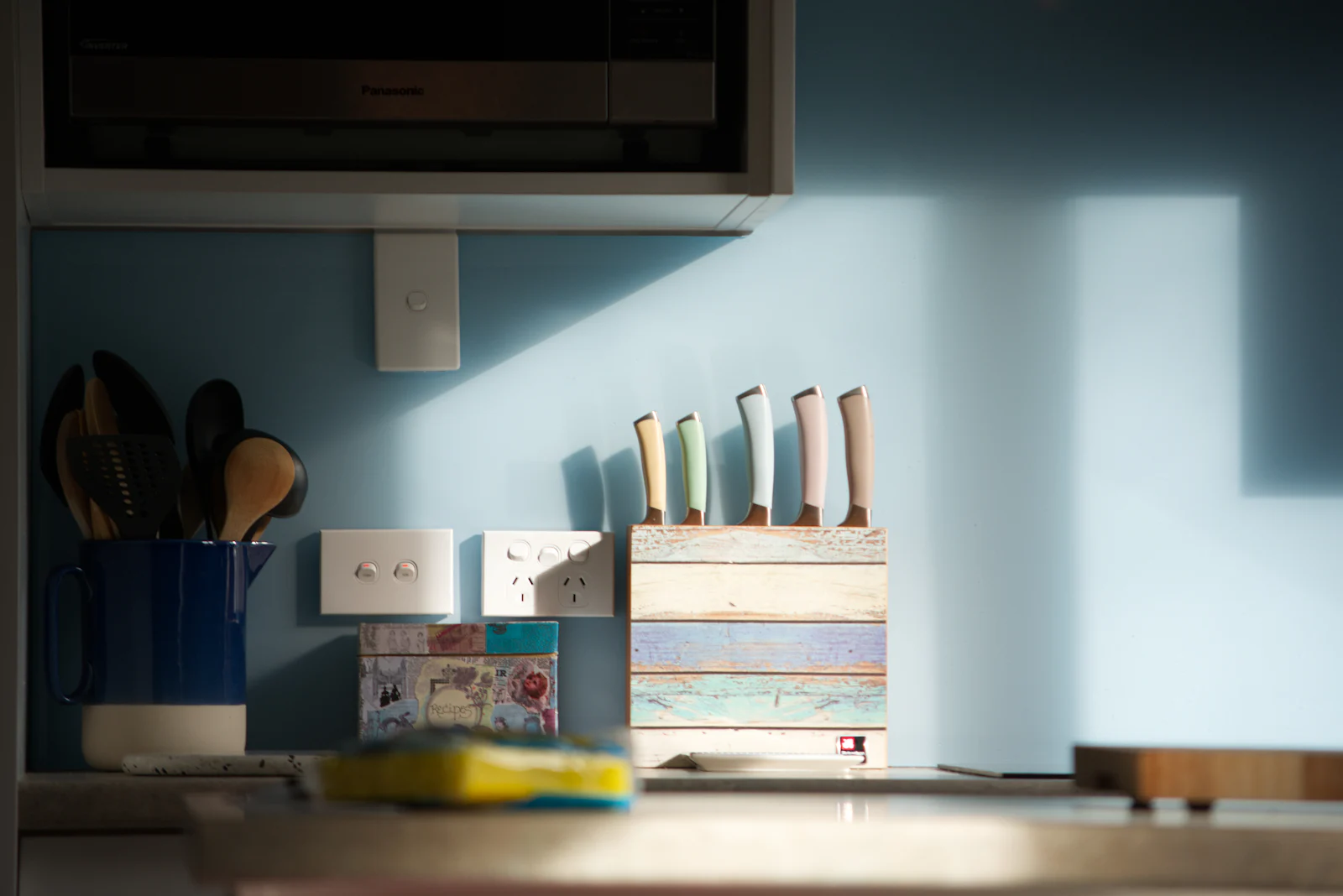 A knife block and utensils against a painted kitchen wall.