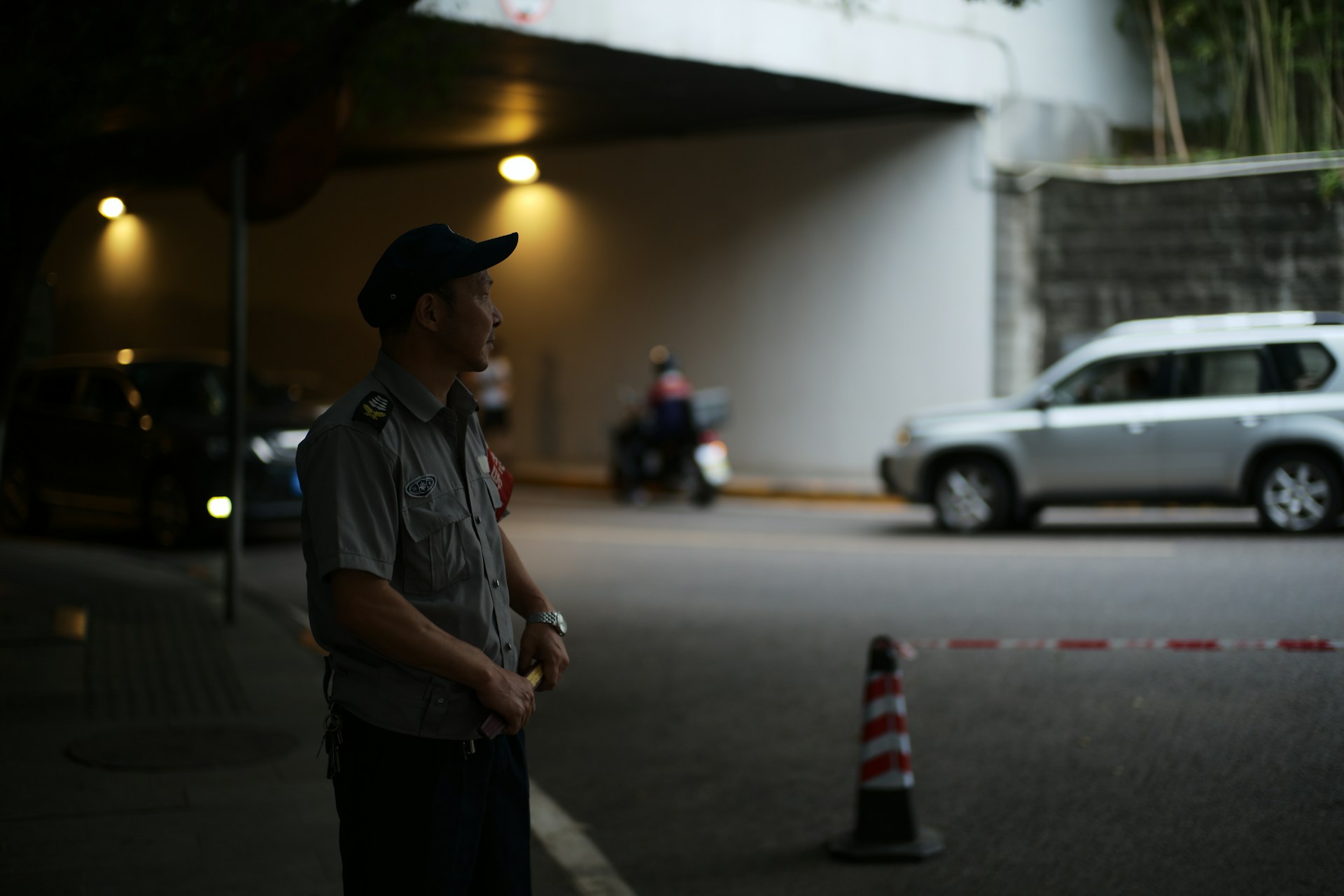 Security guard stands near tunnel entrance with vehicles.