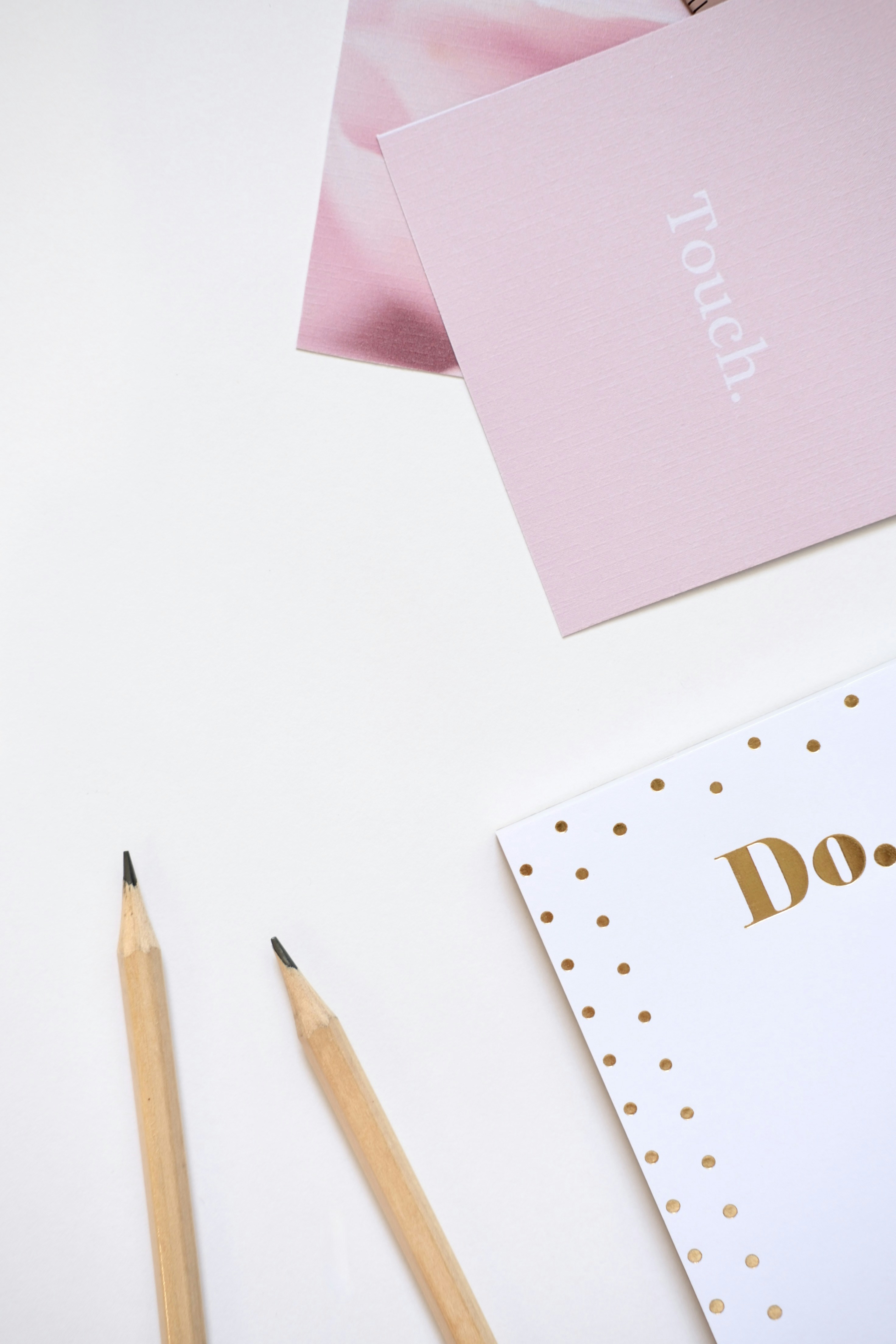 Two pencils and pink notebooks on white surface