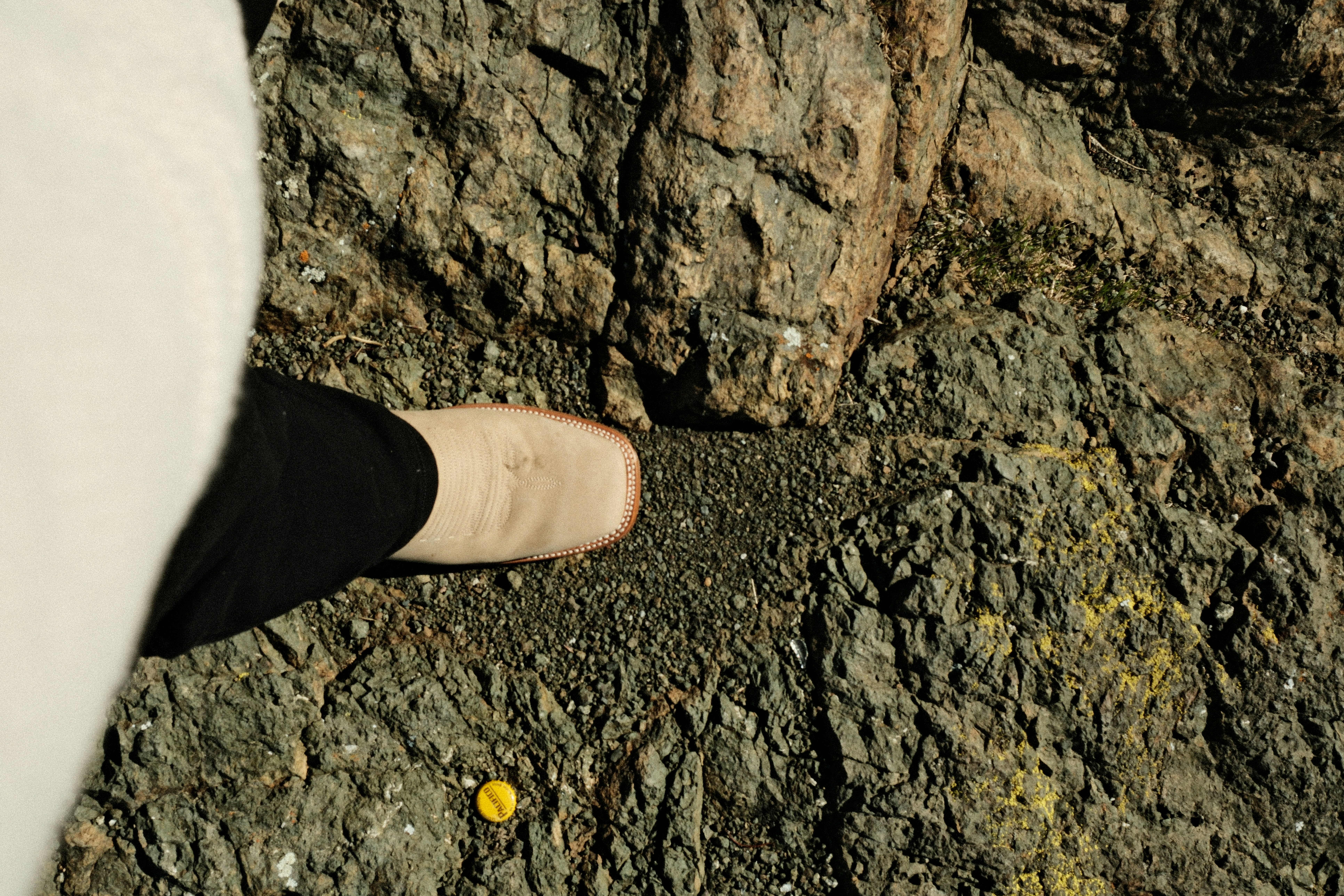 A person's foot steps on gravel near a rock face.