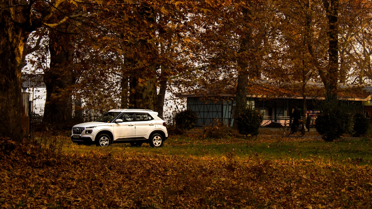 Hvit SUV parkert foran hus med høstfarget løvverk — hyttekjøring