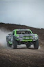 Green off-road racing truck kicking up dust