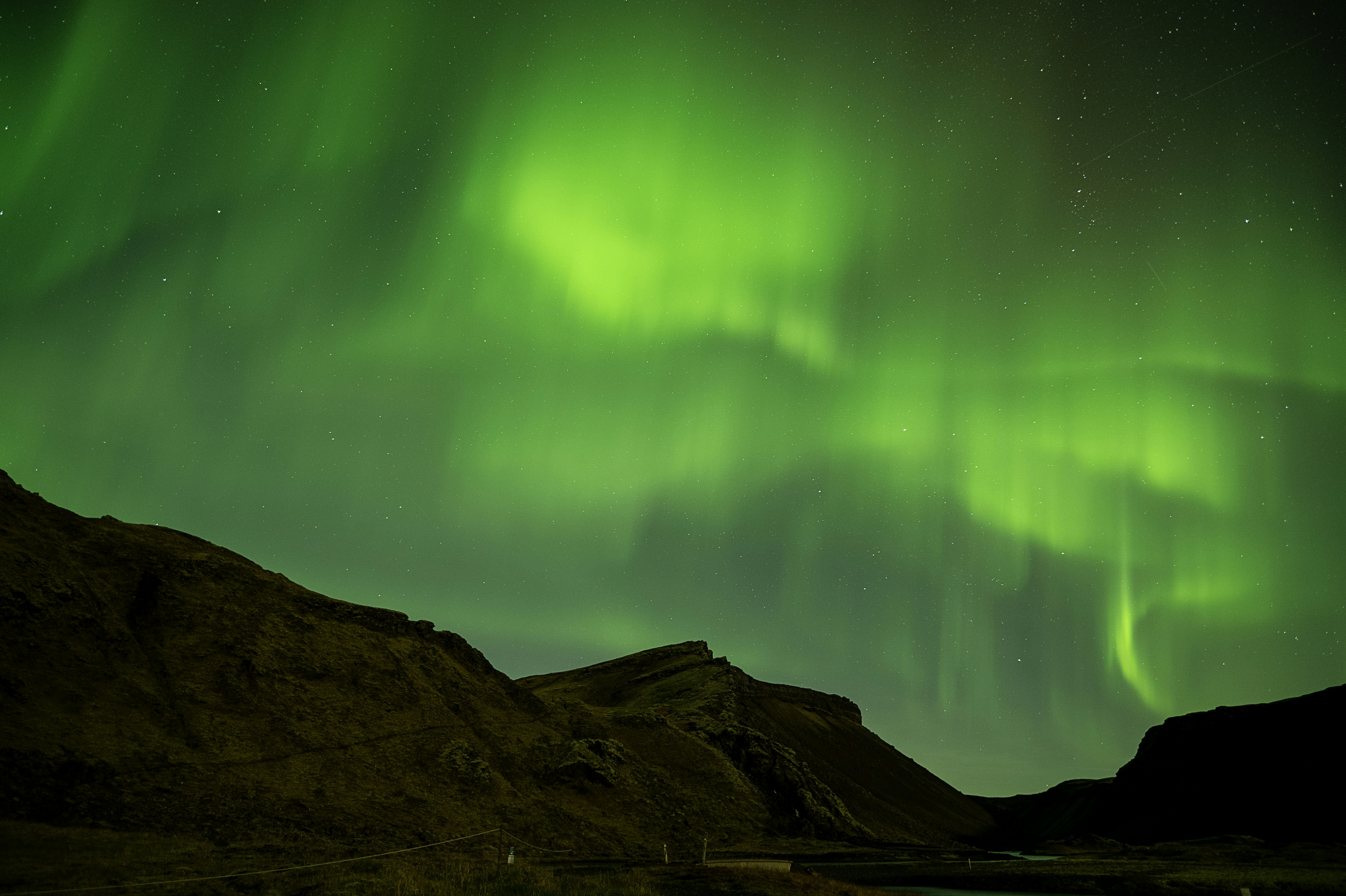 Green aurora borealis over dark mountains at night