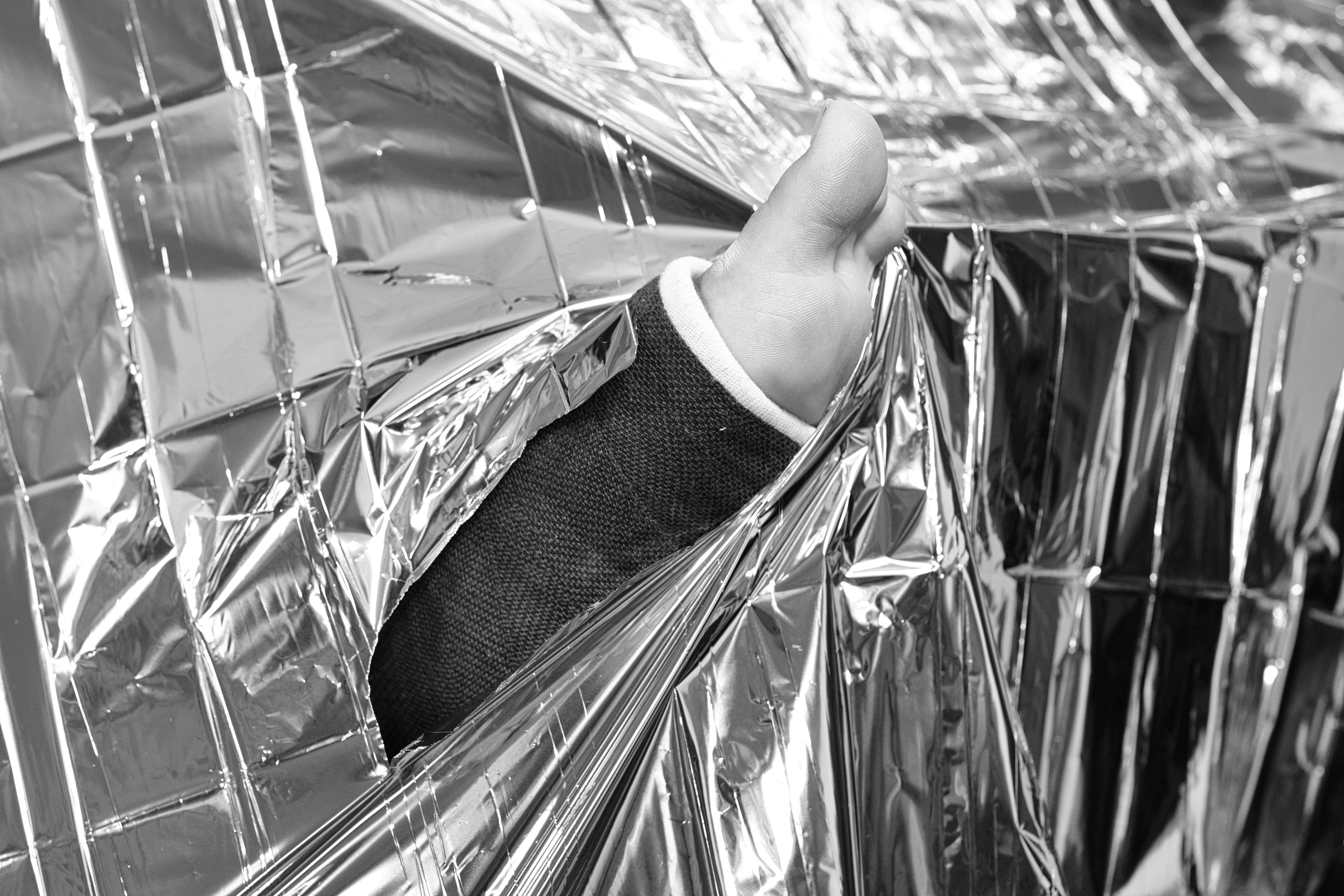 A person's bandaged thumb wrapped in a shiny blanket.