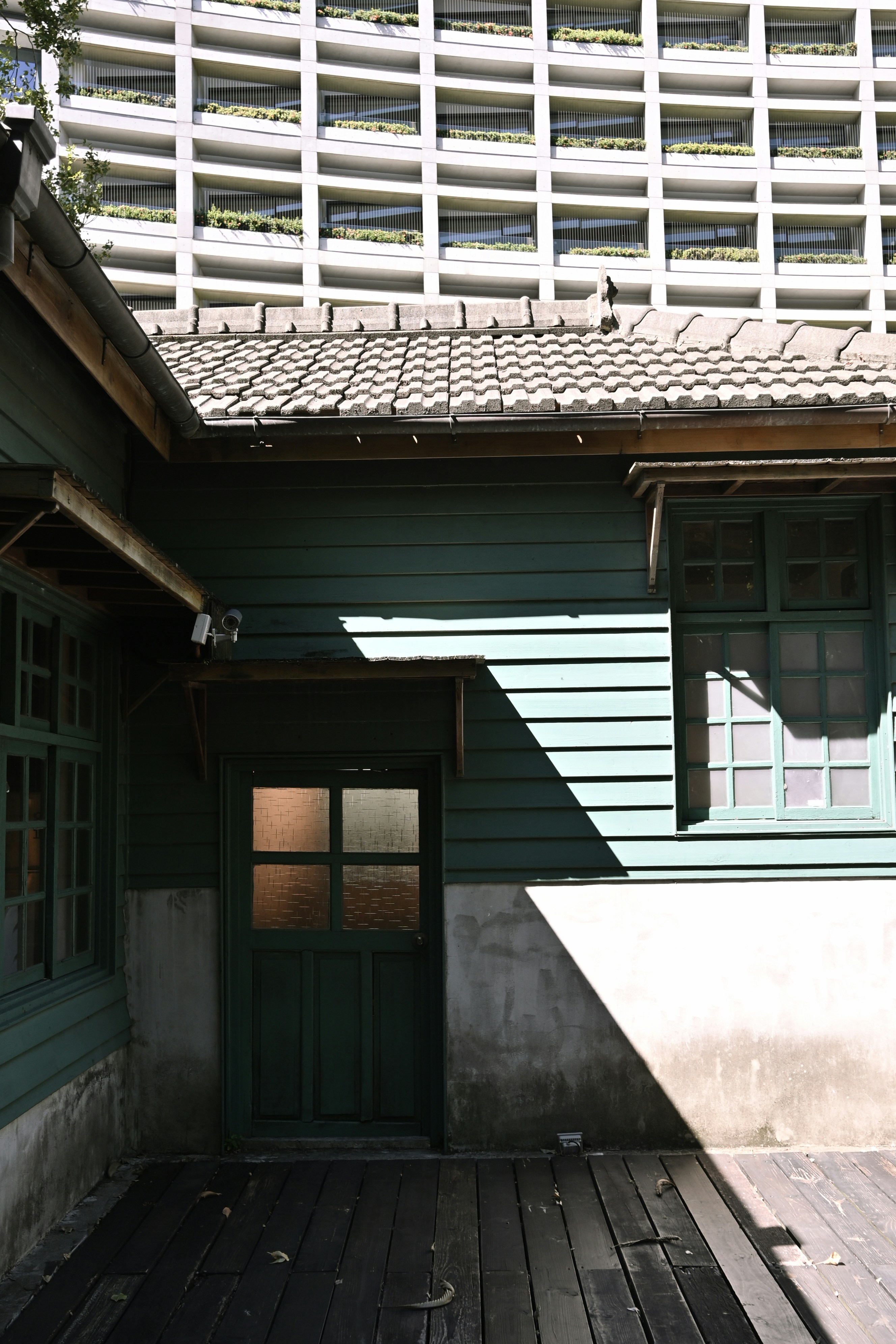 Old green wooden house against modern building