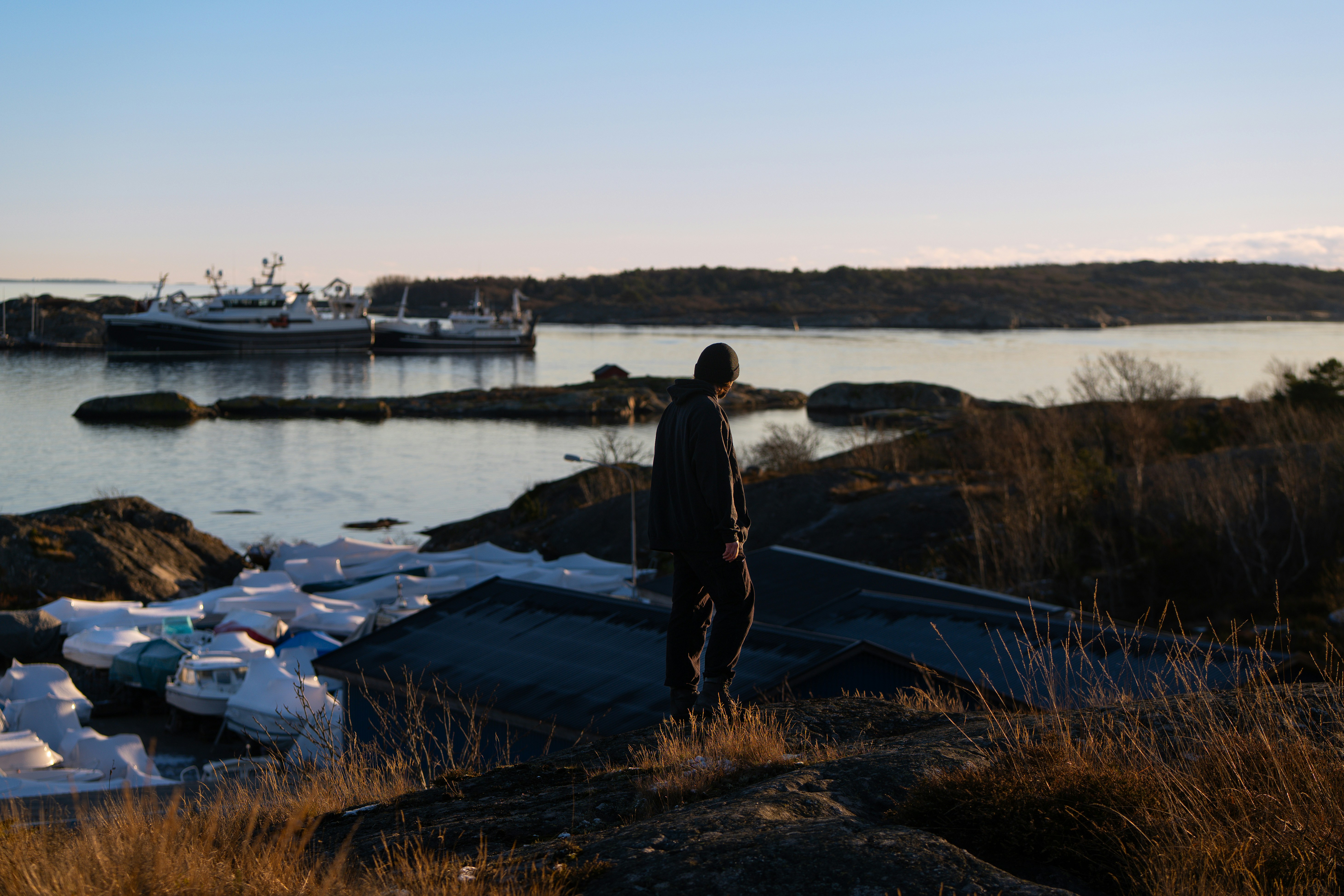 Man standing on rocky shore overlooking harbor.